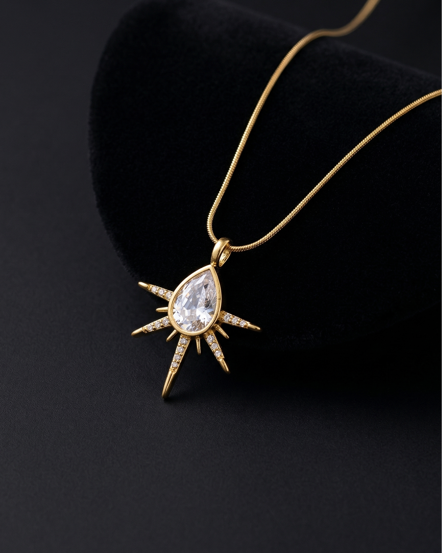Gold necklace with a teardrop-shaped pendant on a black background