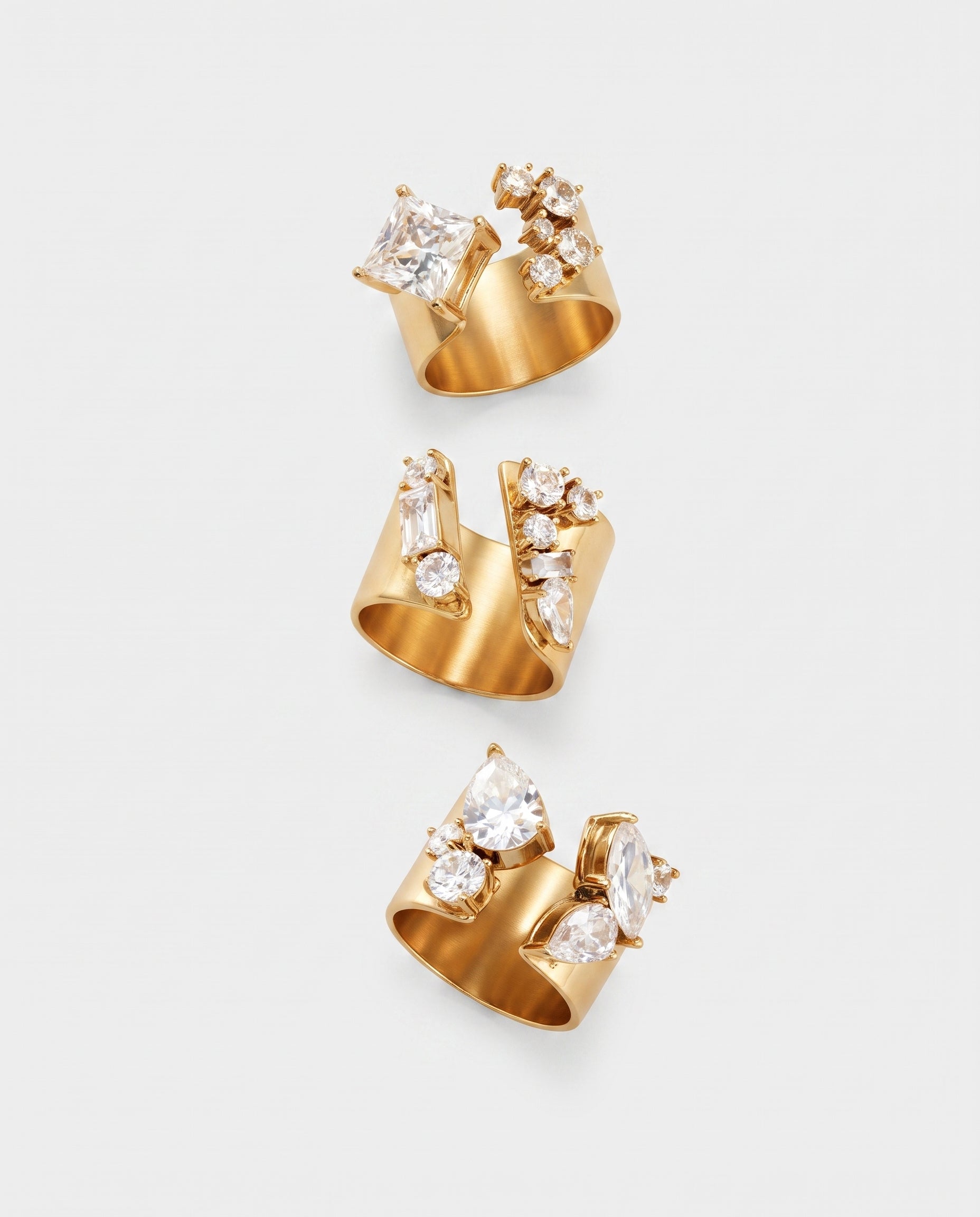 Three gold ring clips with clear gemstones, arranged vertically on a light gray background.