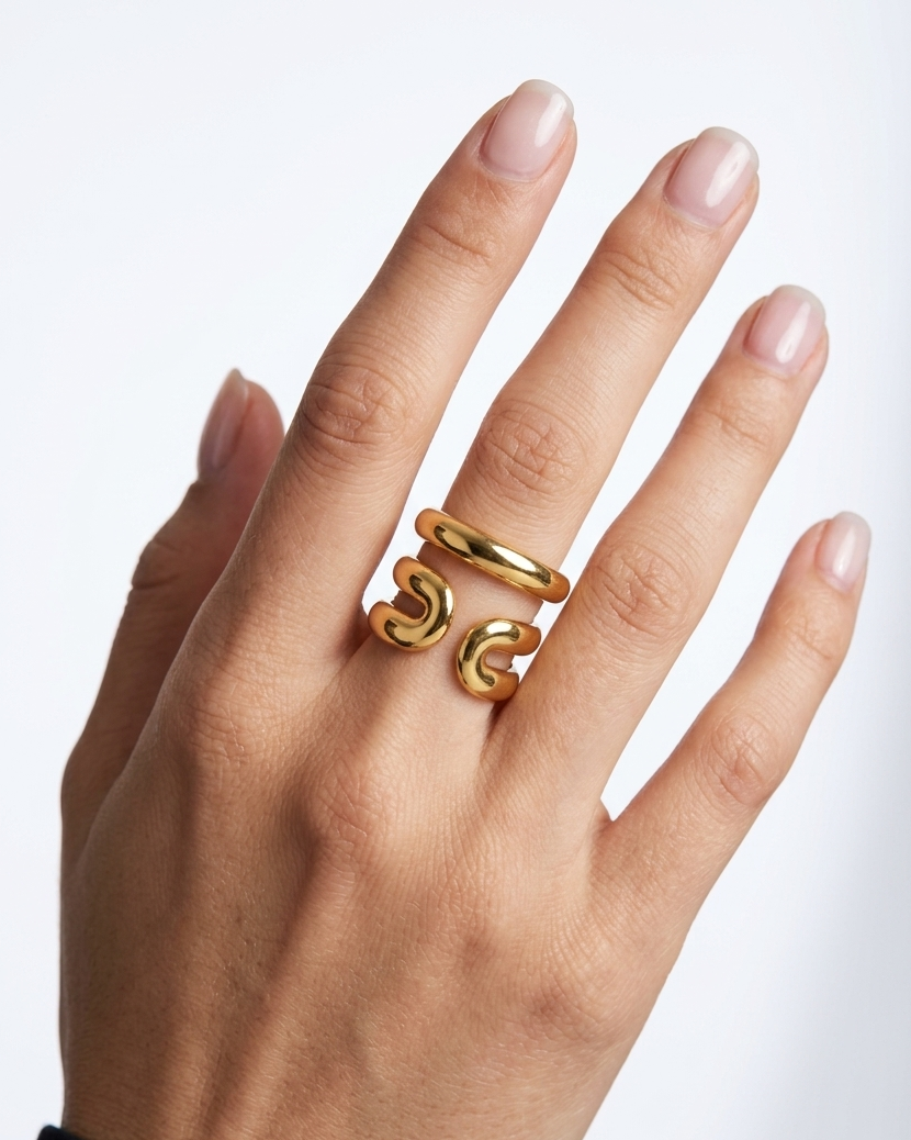 A close-up of a hand wearing two interlocking gold rings, one smooth and one textured, against a clean white background.