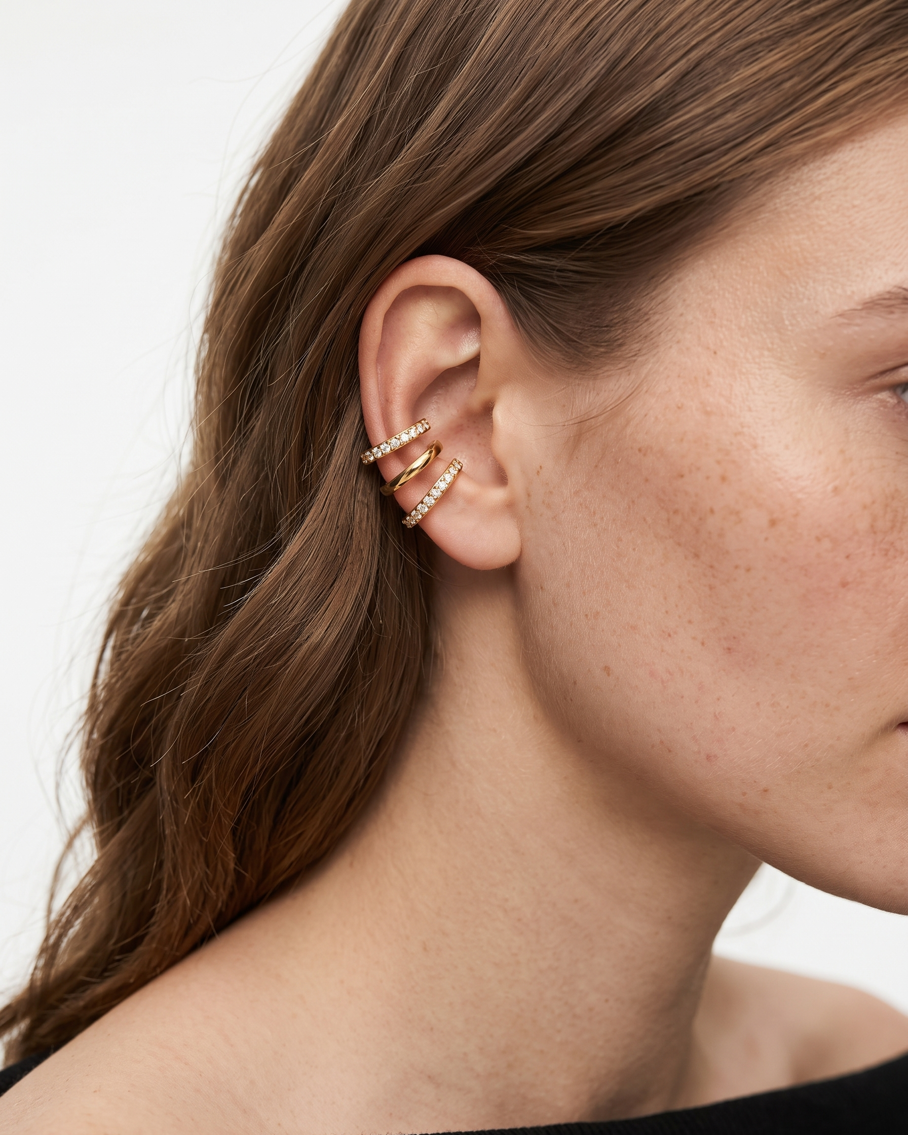 Close-up of a woman's ear wearing a gold earring with a white background