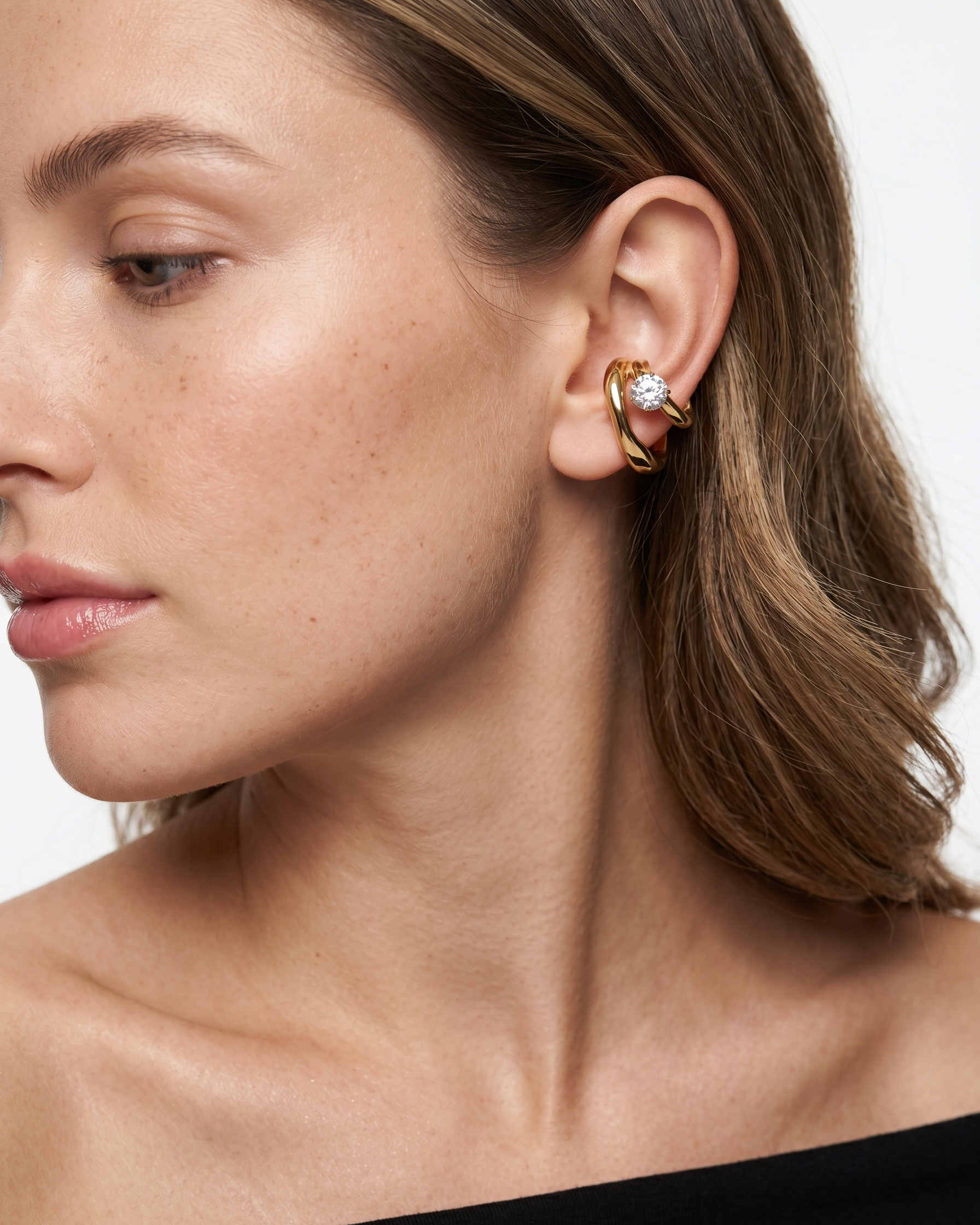 Close-up of a woman wearing a gold earring with a clear gemstone on a neutral background