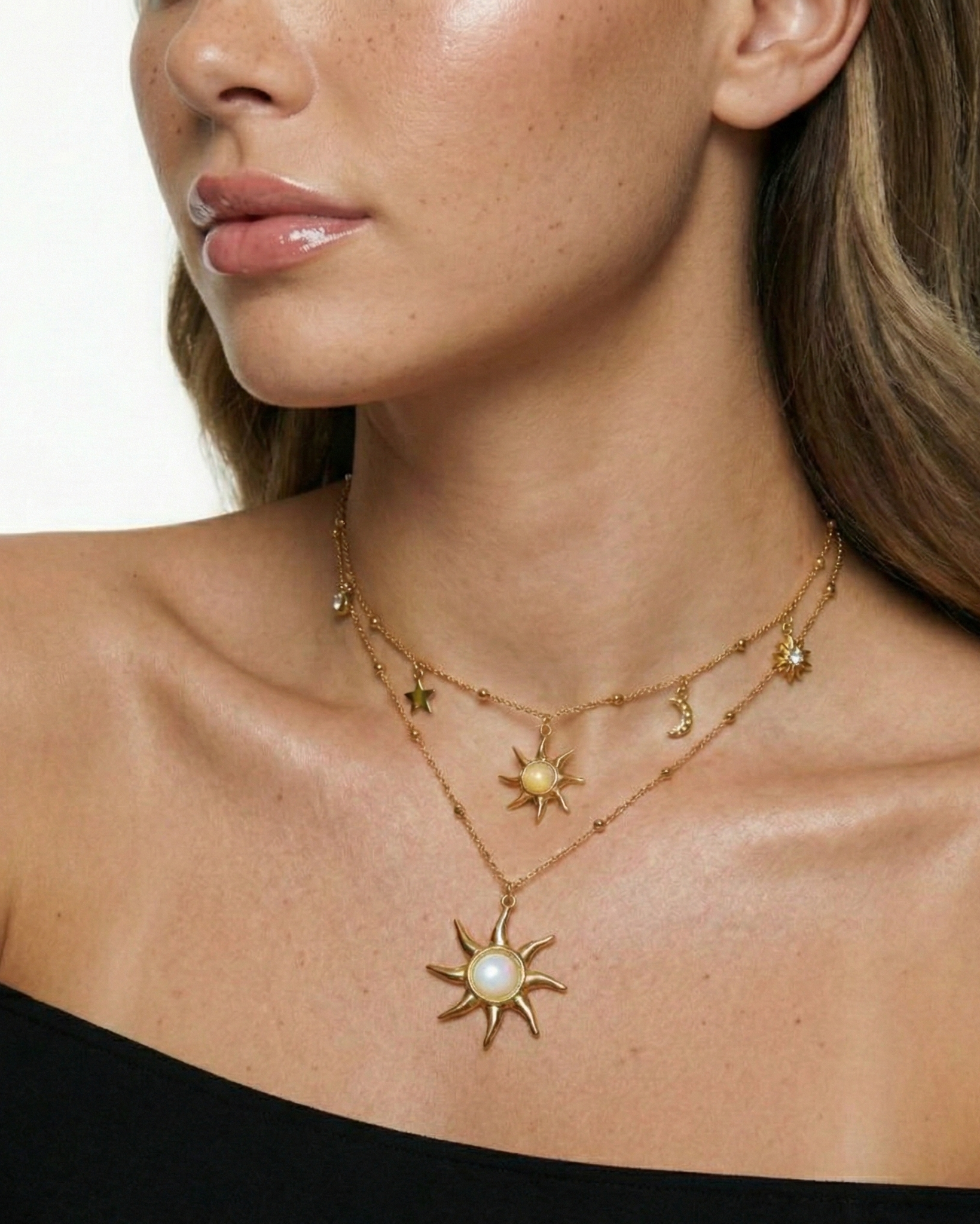 Close-up of a woman wearing a gold necklace with sun-shaped pendants on a white background