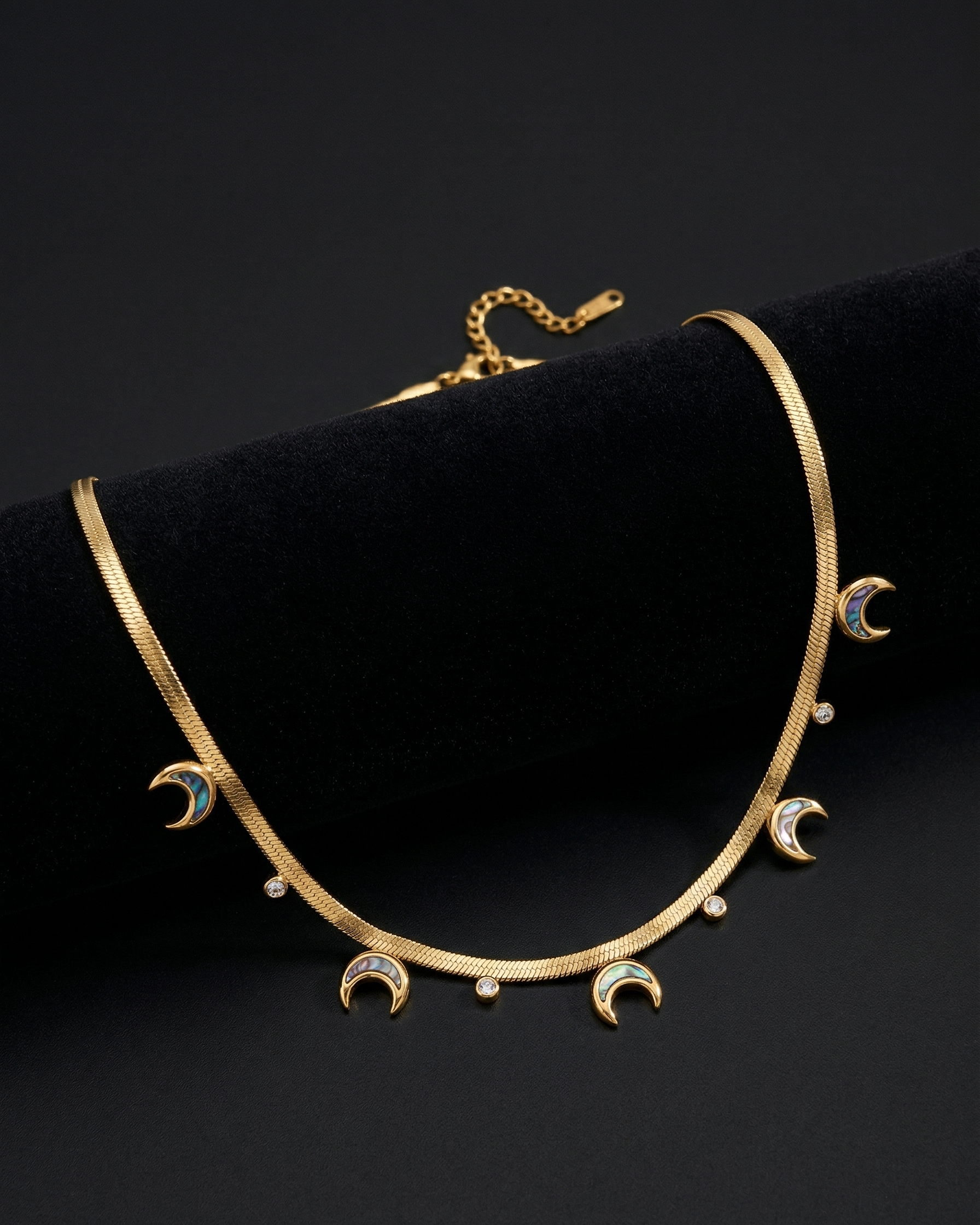 Gold necklace with moon and star designs on a black background