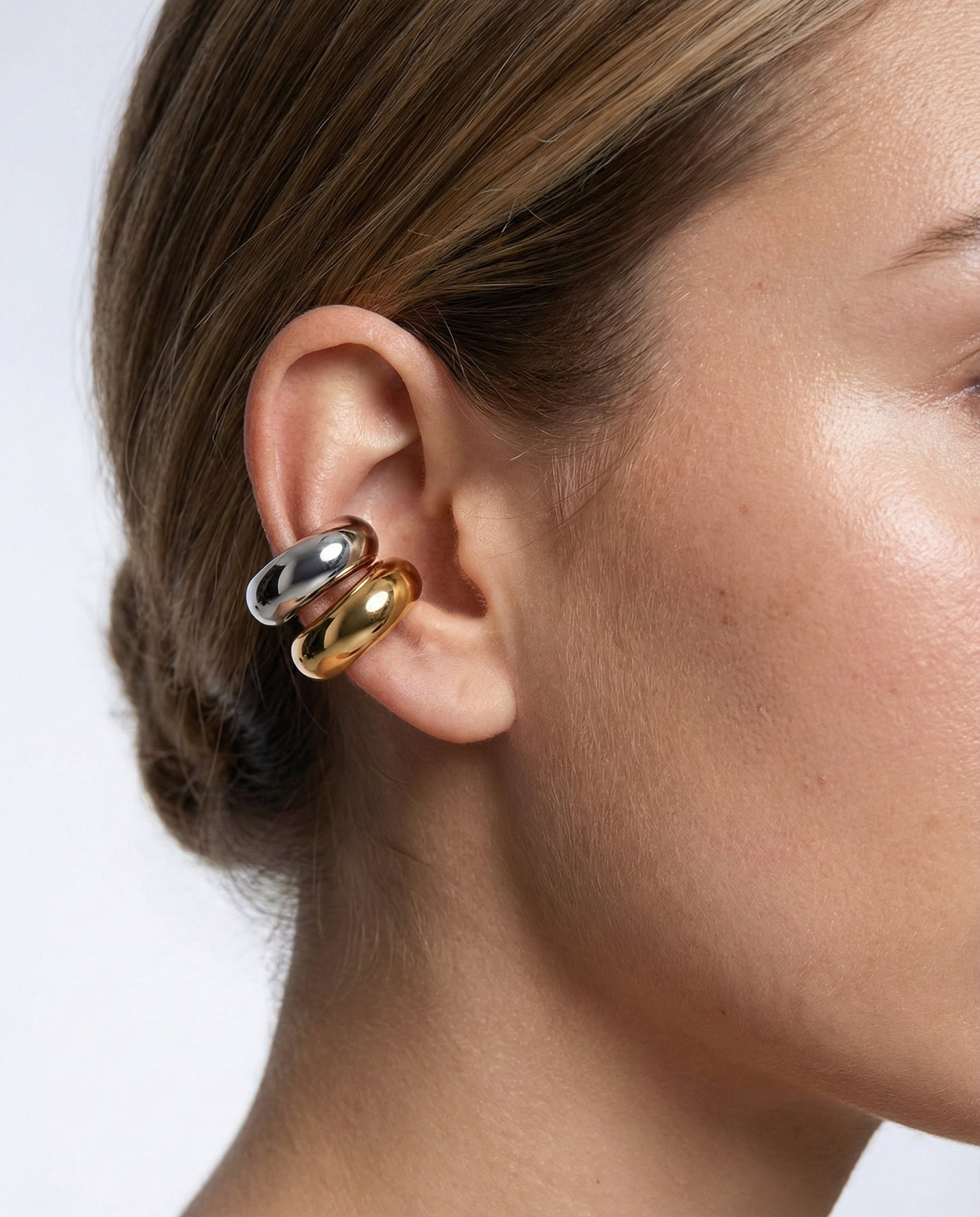 Close-up of a person wearing a gold and silver earring on a white background
