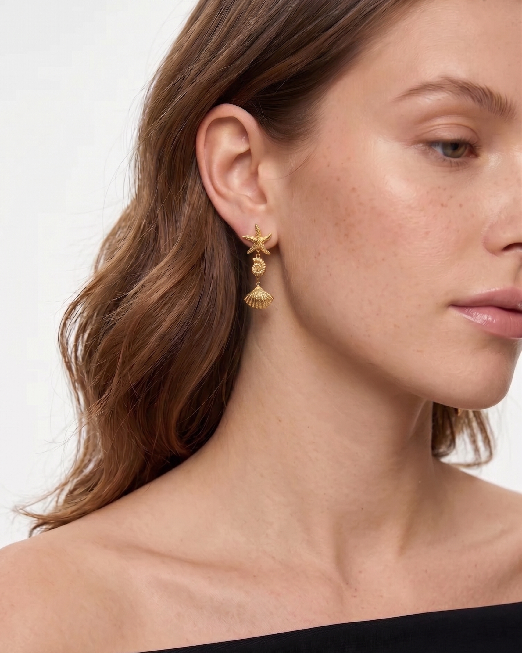 Close-up of a woman wearing gold earrings with a plain background