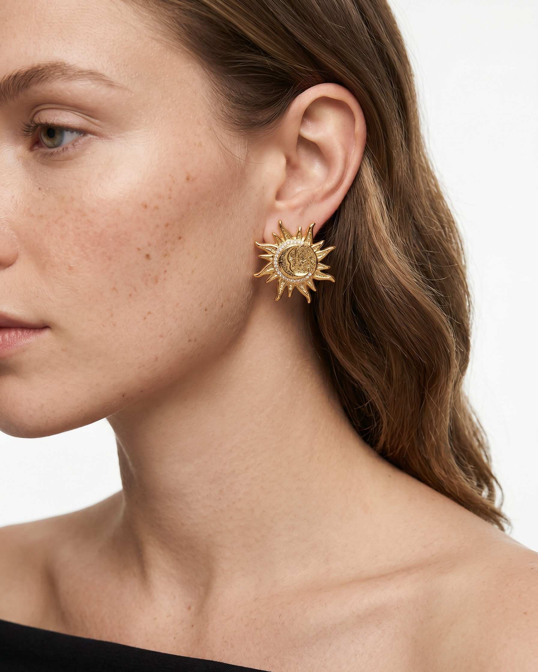 Close-up of a woman wearing gold sun-shaped earrings on a white background