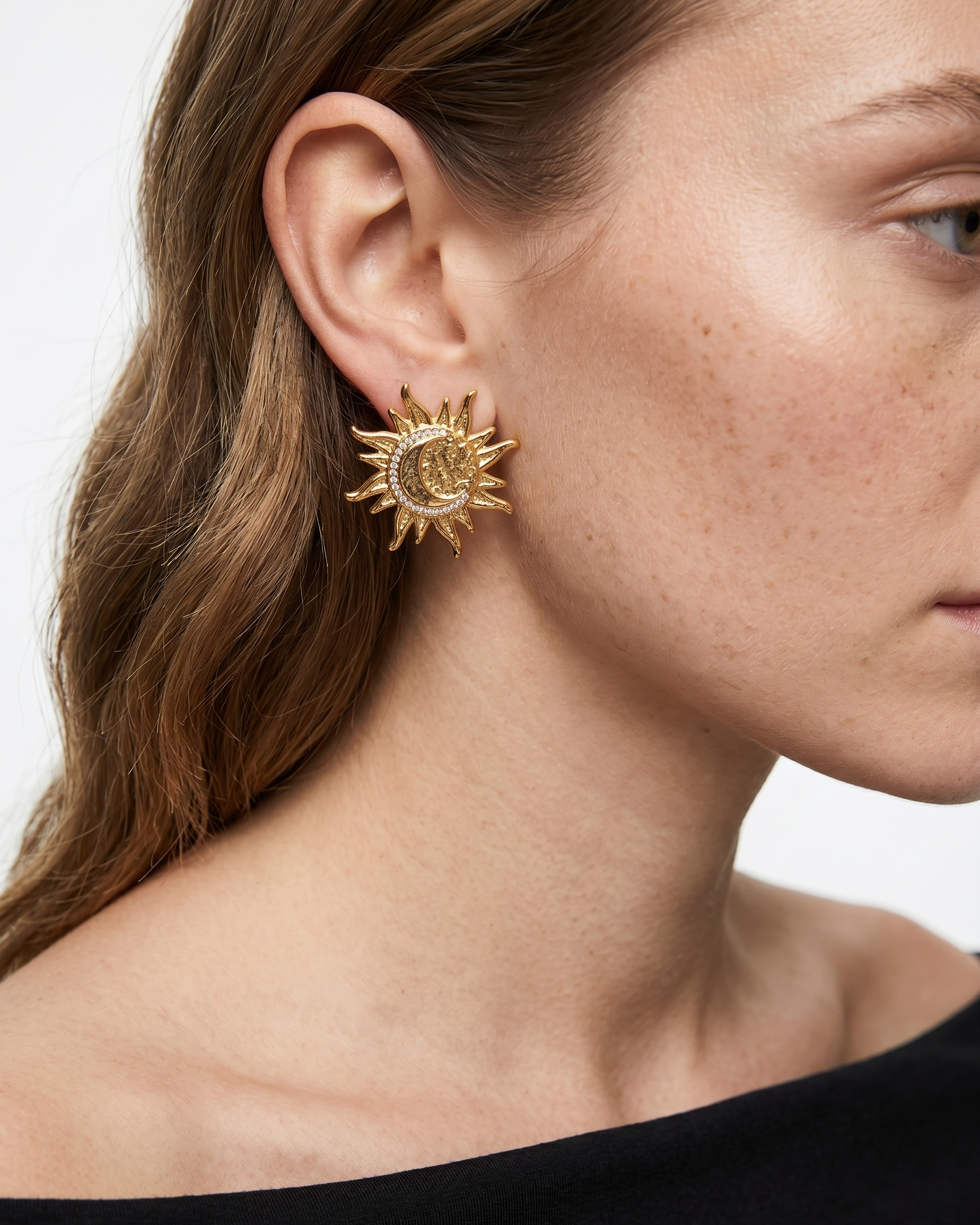 Close-up of a person wearing a gold sun-shaped earring on a plain background