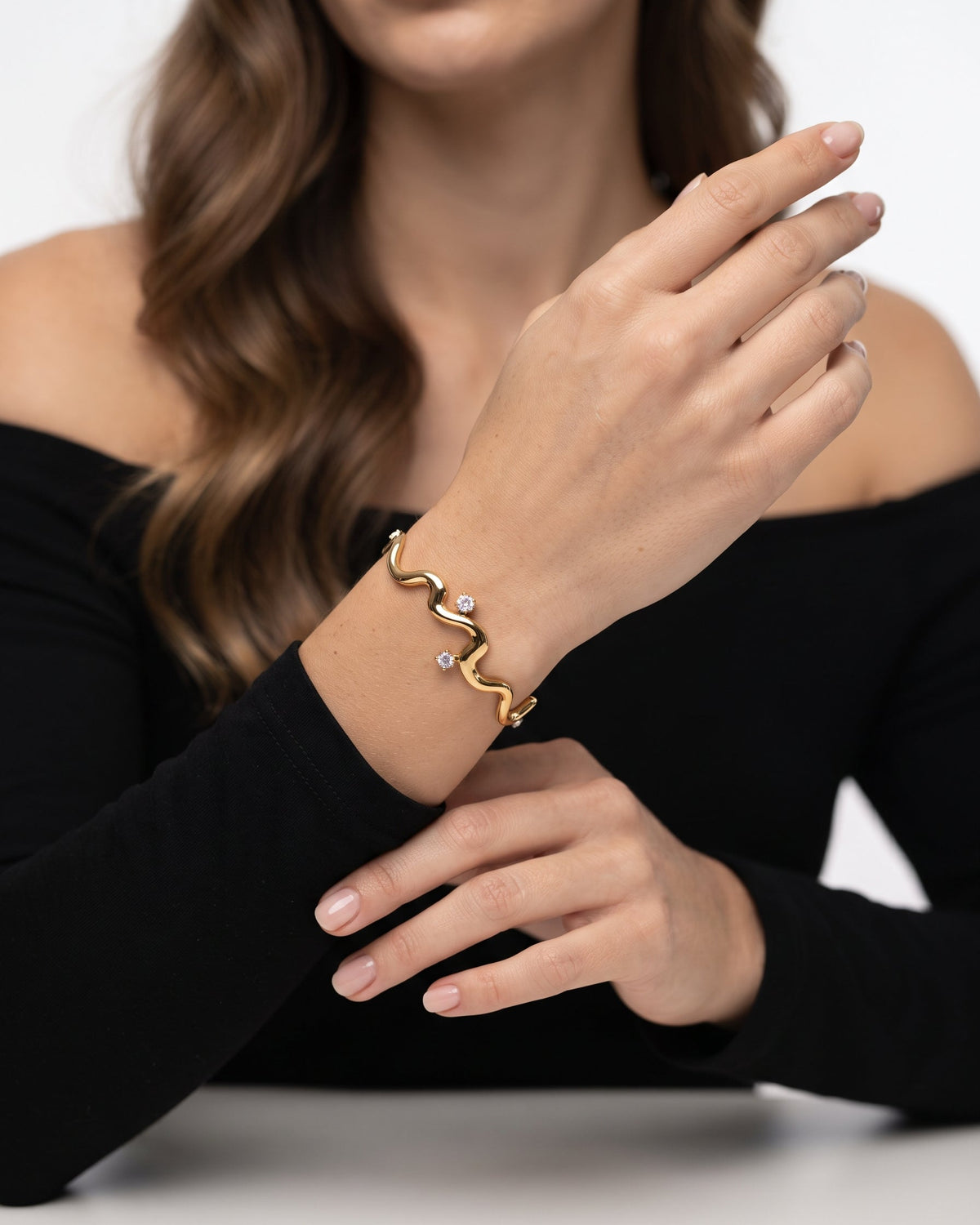 A gold wavy bracelet with small clear crystal accents worn on a model's wrist, shown against a clean white background.