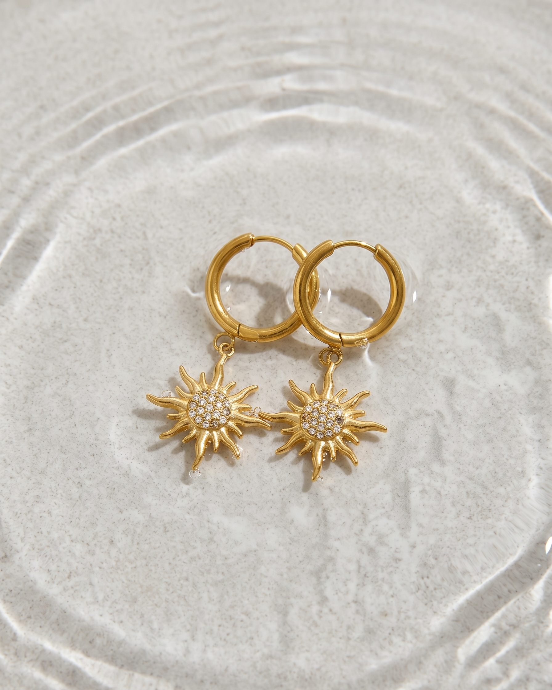 Gold hoop earrings with sunflower-shaped charms on a textured beige surface