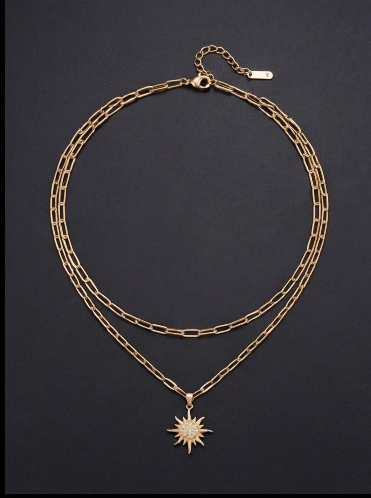 Gold chain necklace with a sun pendant on a dark background