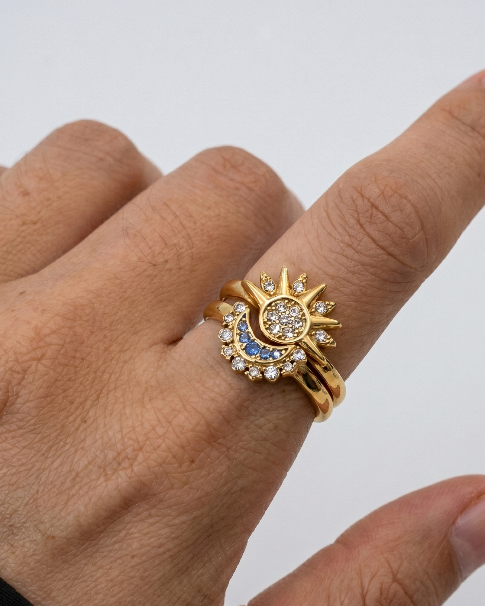 Gold ring with gemstones on a person's finger against a white background