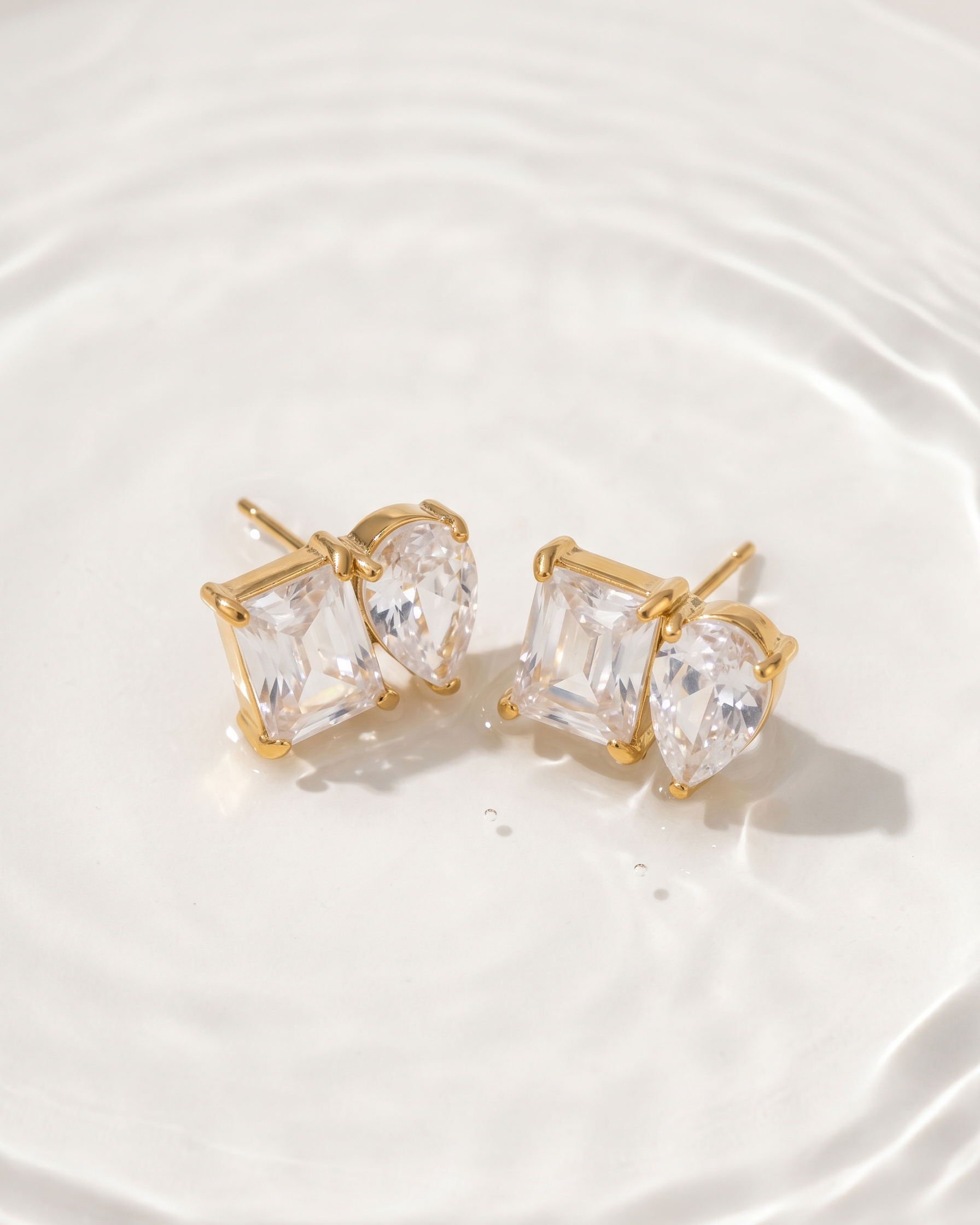 Gold earrings with clear gemstones on a white plate