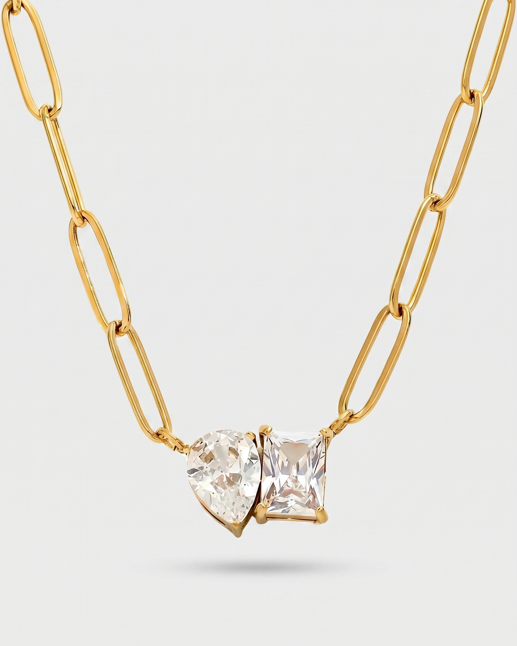 Gold chain necklace with a heart-shaped clear gemstone on a light gray background