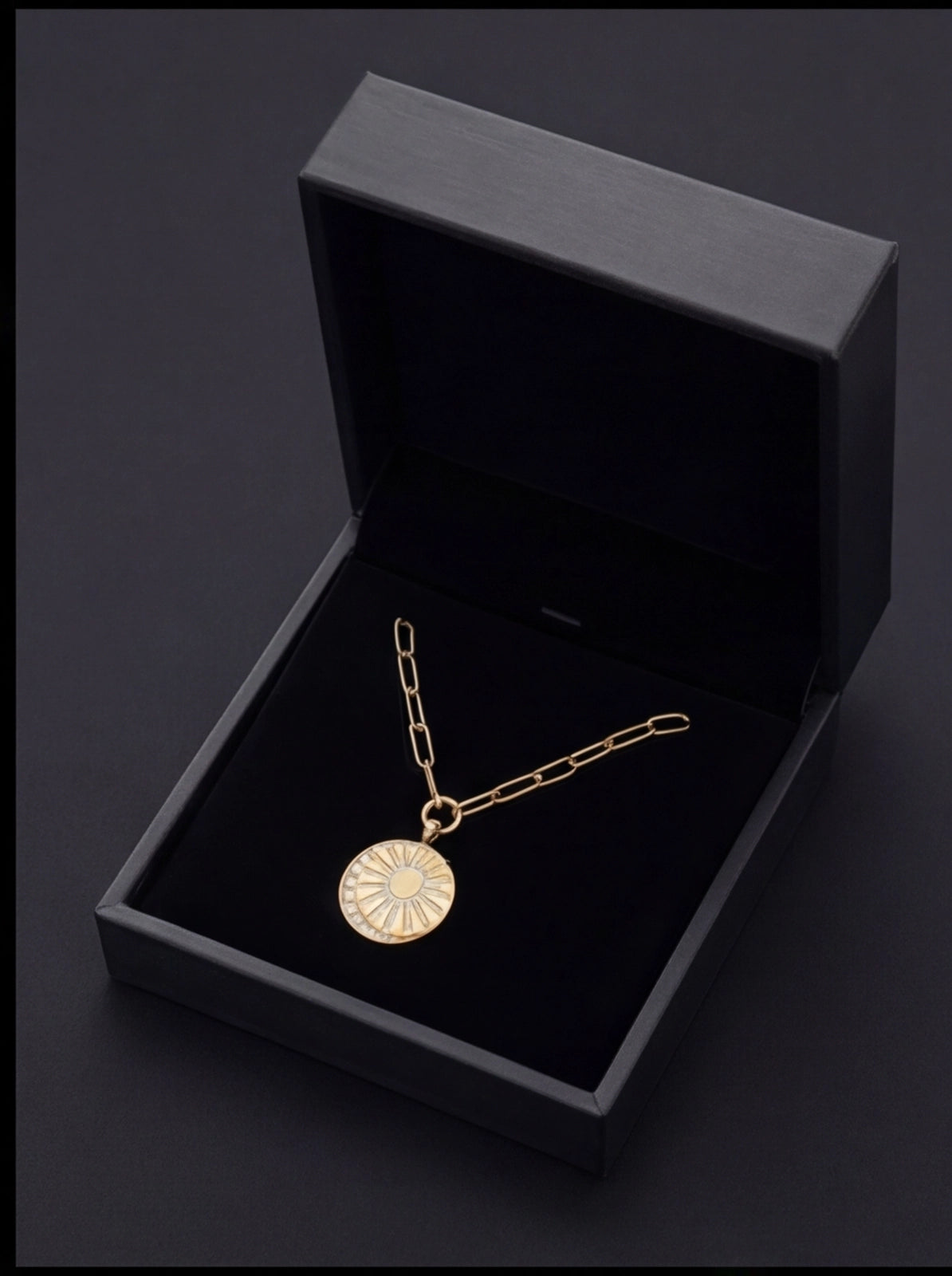 Gold necklace with a circular pendant in an open black jewelry box on a dark background