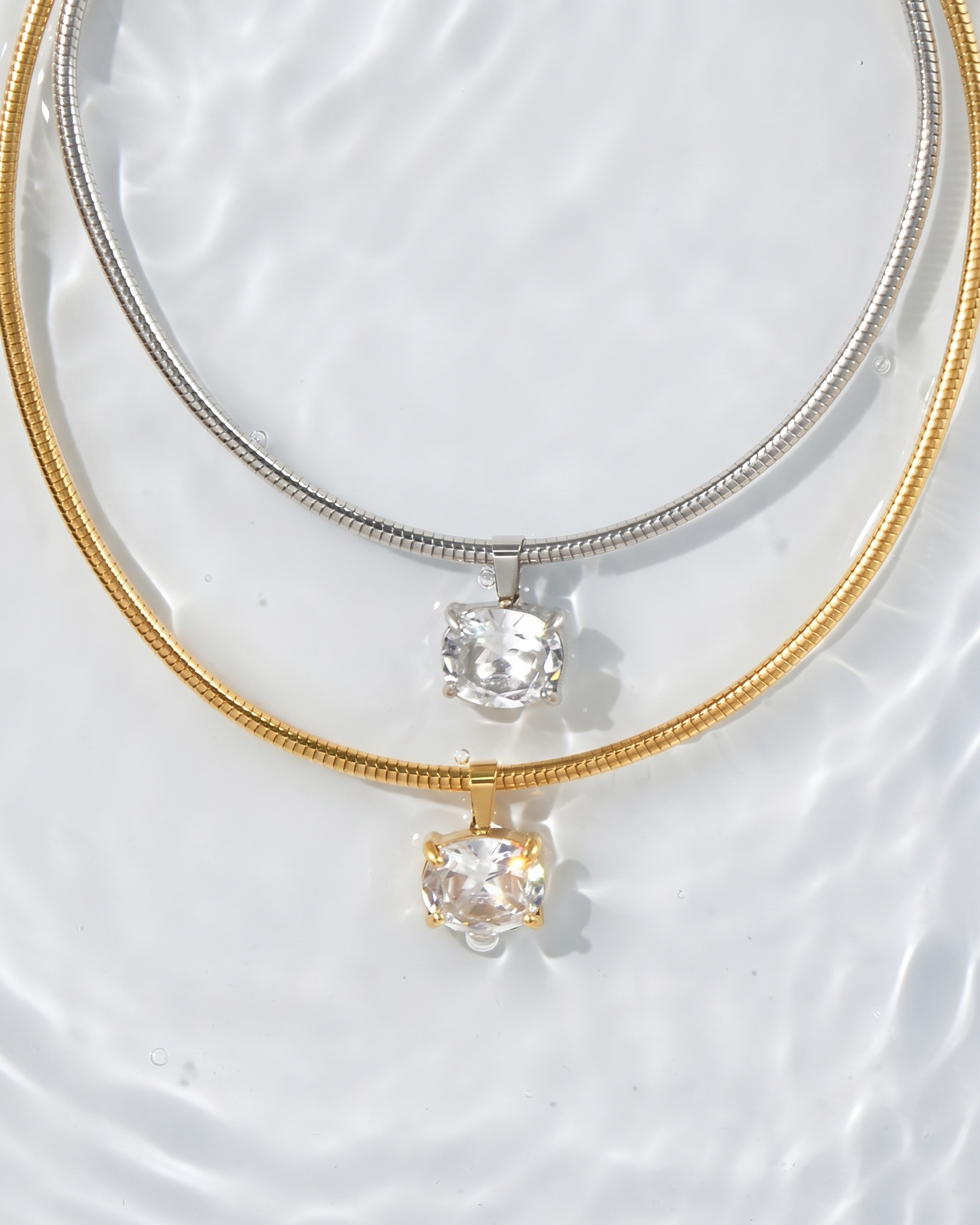 Two gold necklaces with clear gemstones on a textured white surface
