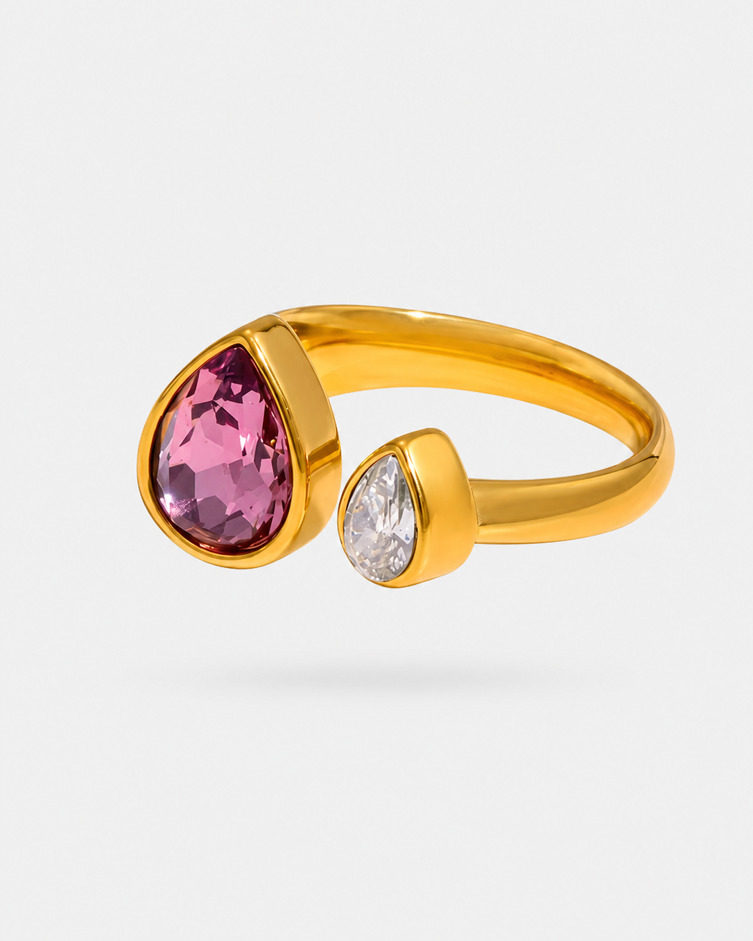 A gold ring with a large faceted pink teardrop gemstone and a smaller clear teardrop gemstone, shown on a light gray background.