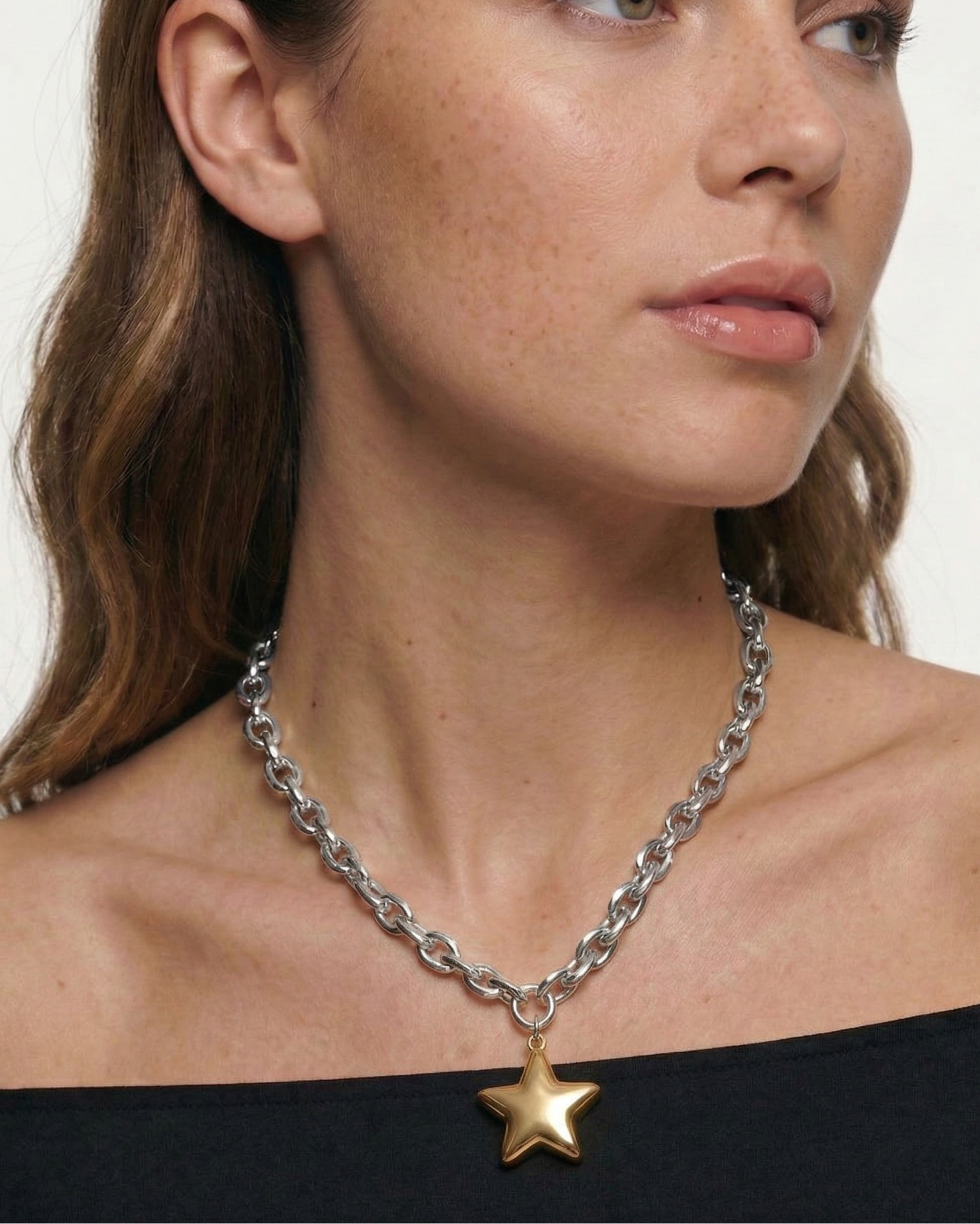 Woman wearing a silver chain necklace with a star pendant on a plain background