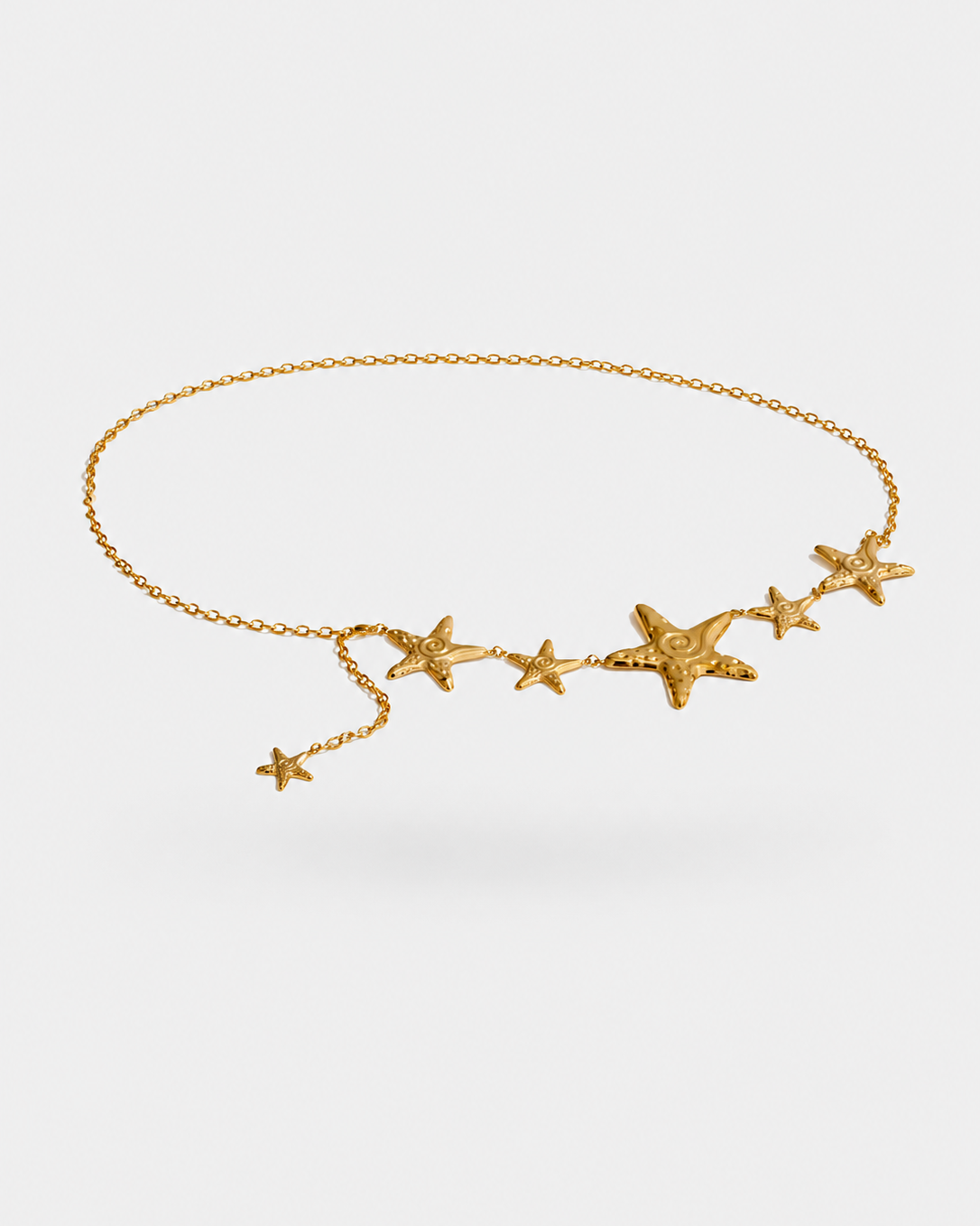 A delicate gold chain accessory featuring five textured starfish charms in various sizes, displayed on a clean light gray background.