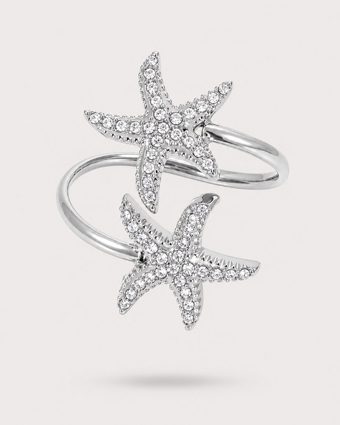 A silver-toned wrap ring featuring two starfish motifs paved with small clear stones, shown on a light gray background.