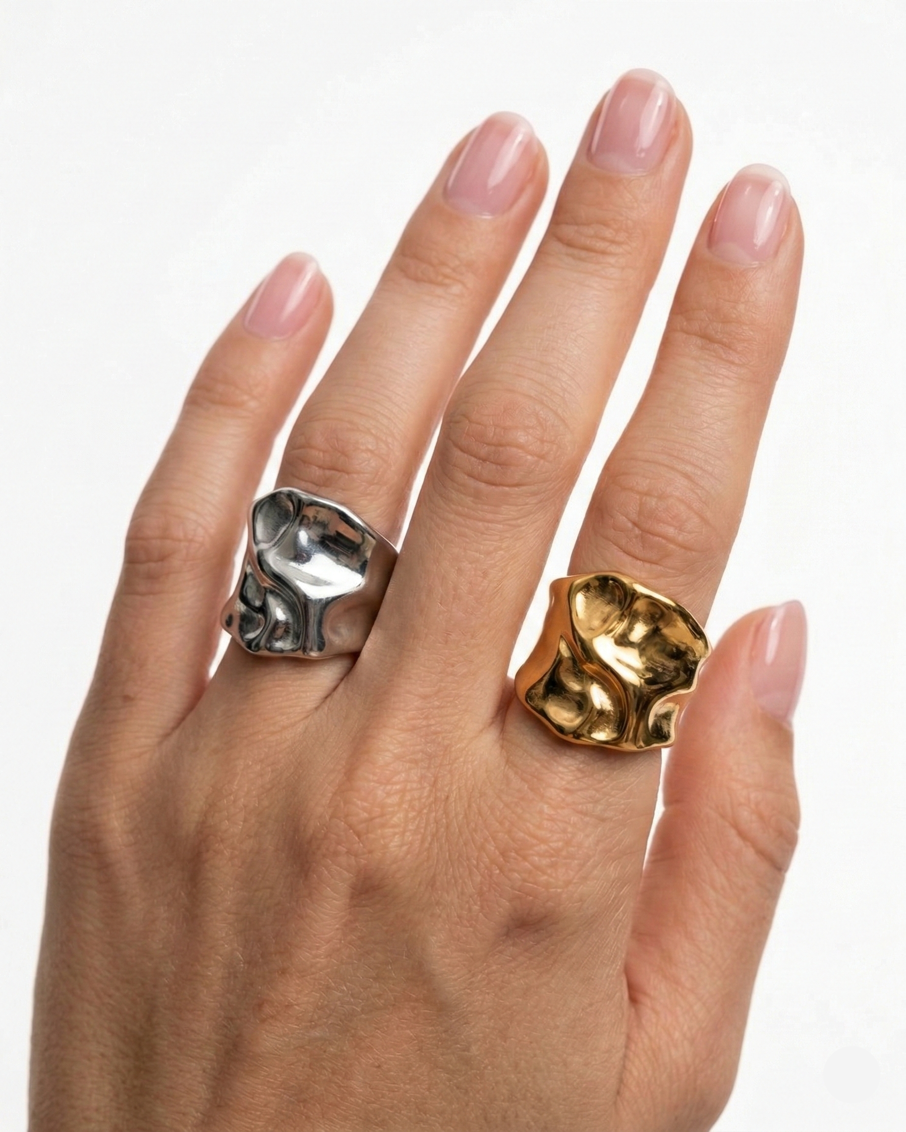 Hand wearing two rings, one gold and one silver, on a white background