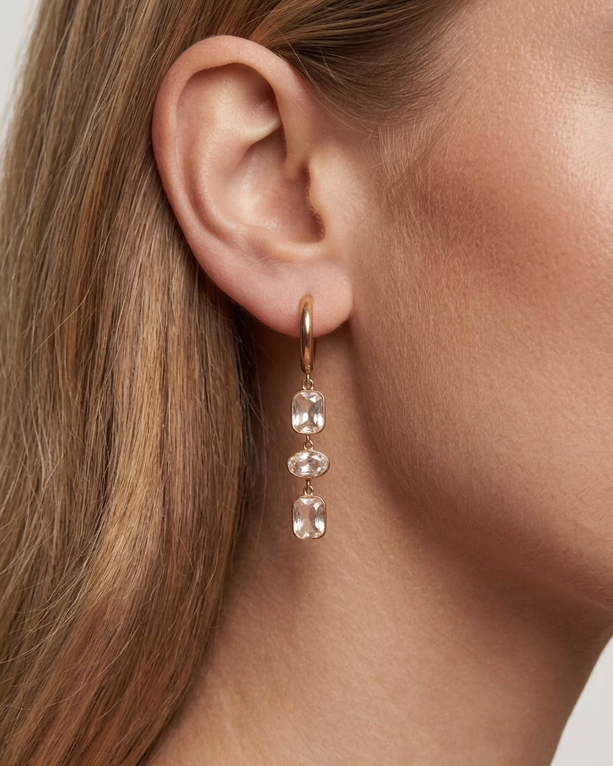 Close-up of an ear wearing a gold earring with clear gemstones.