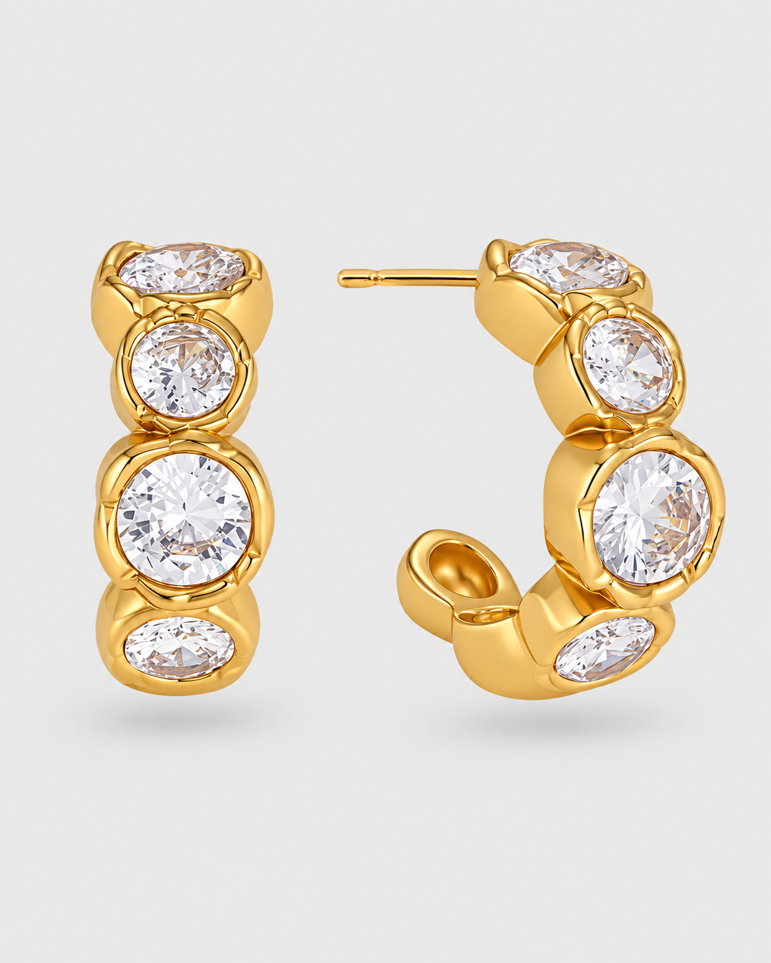 Gold hoop earrings with bezel-set round and oval clear gemstones, shown on a light gray background.