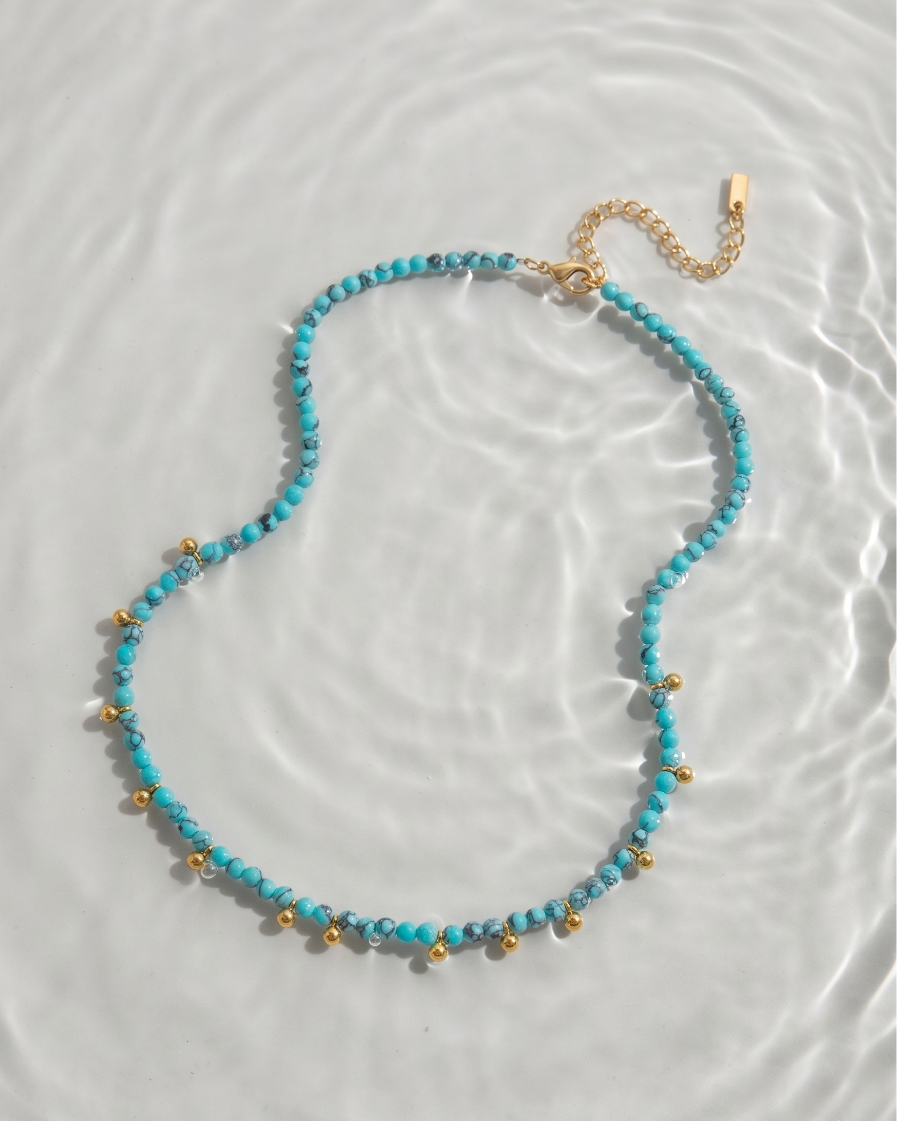 Necklace with blue beads and gold accents on a light gray background