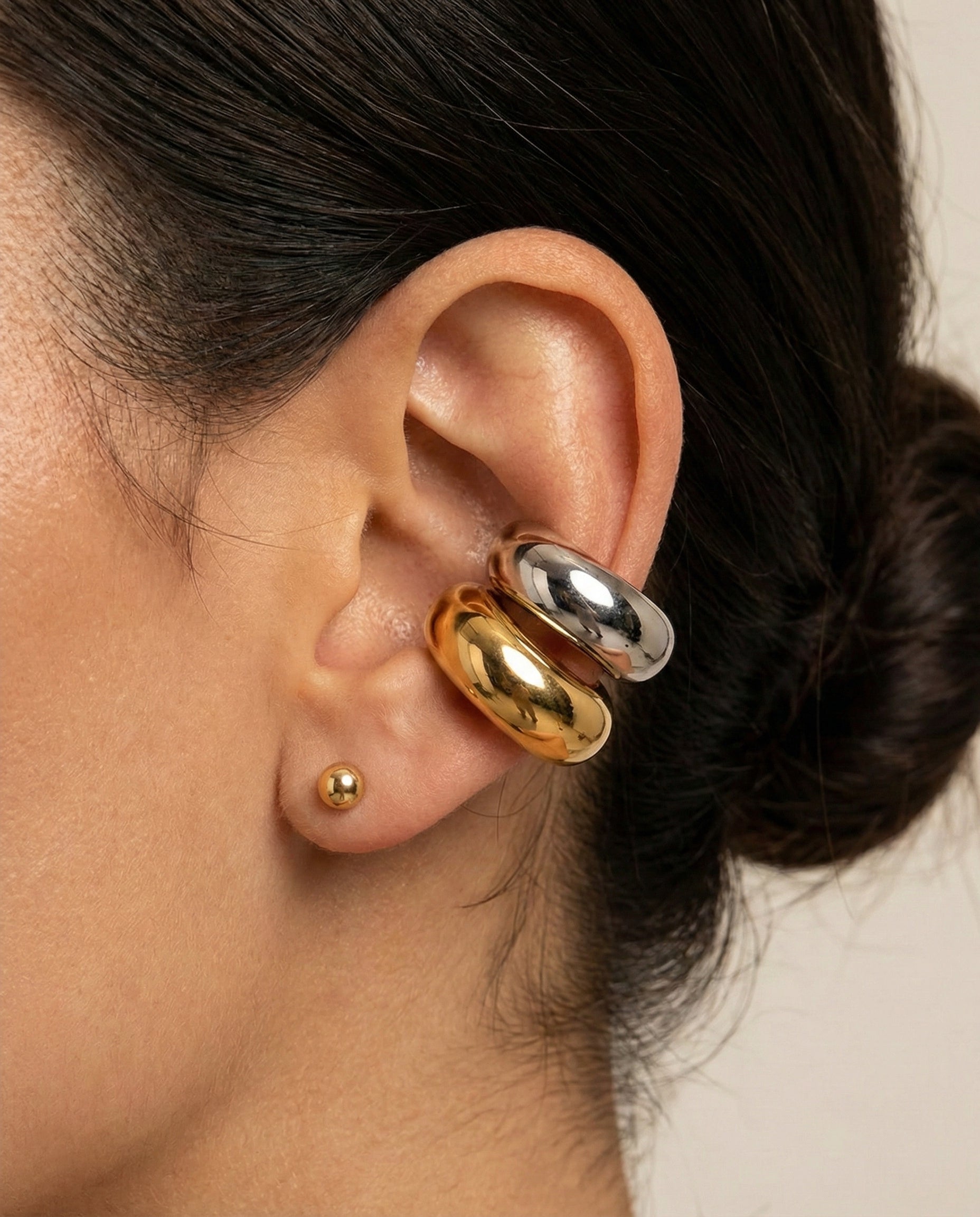 Close-up of an ear wearing gold and silver hoop earrings with a blurred background