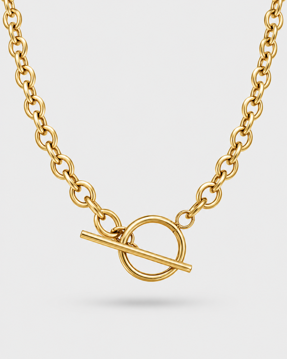 A gold chain necklace with a toggle clasp featuring a circular ring and a diagonal bar, shown on a light gray background.