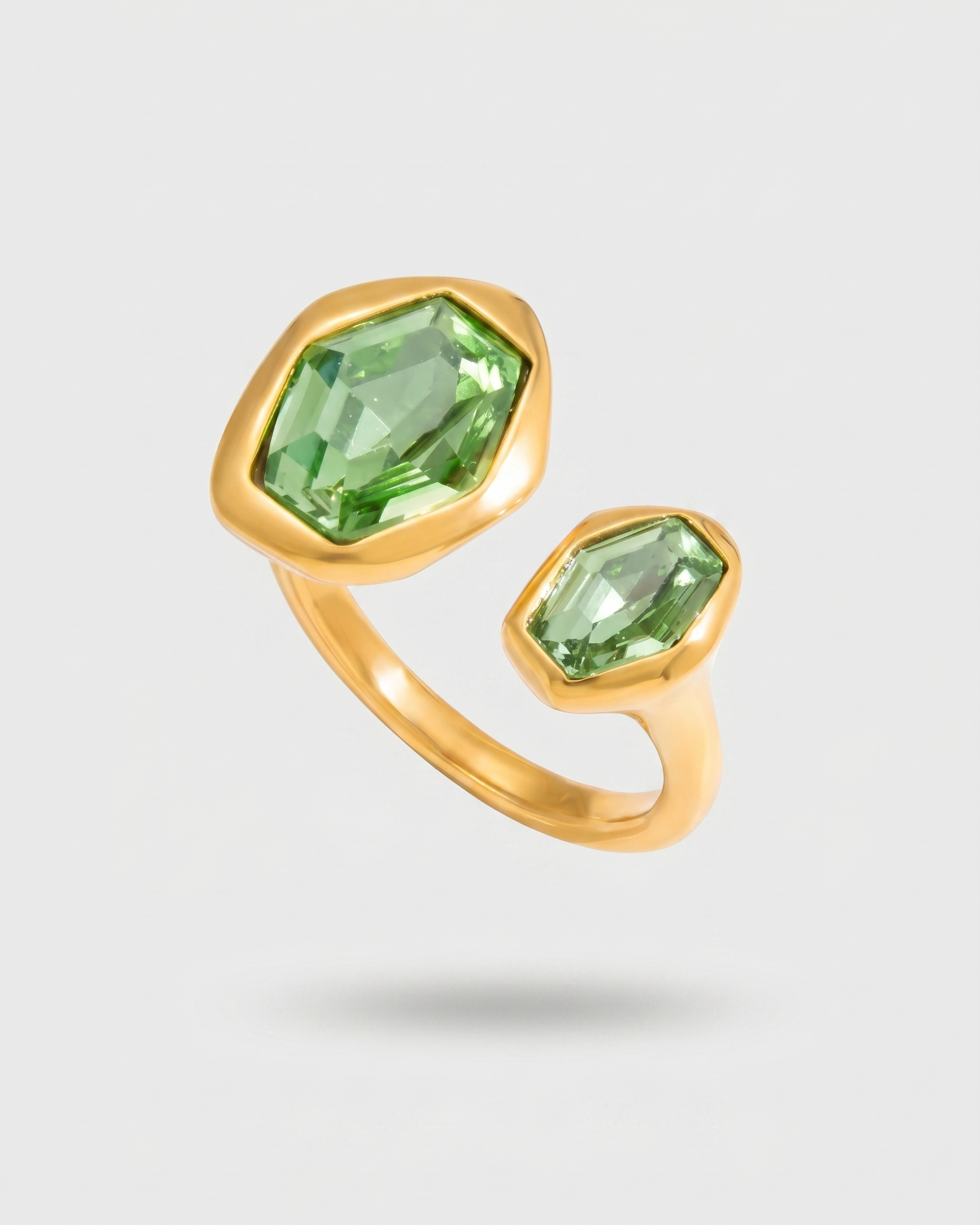 Gold ring with green gemstones on a light gray background
