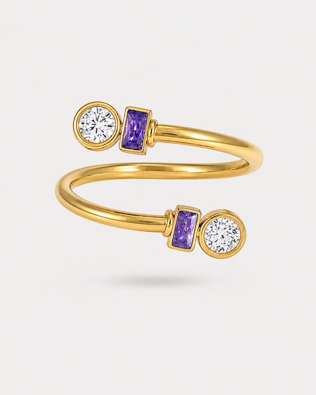 A gold wrap ring featuring two purple rectangular baguette-cut gemstones and two round-cut clear gemstones, displayed on a light gray background.