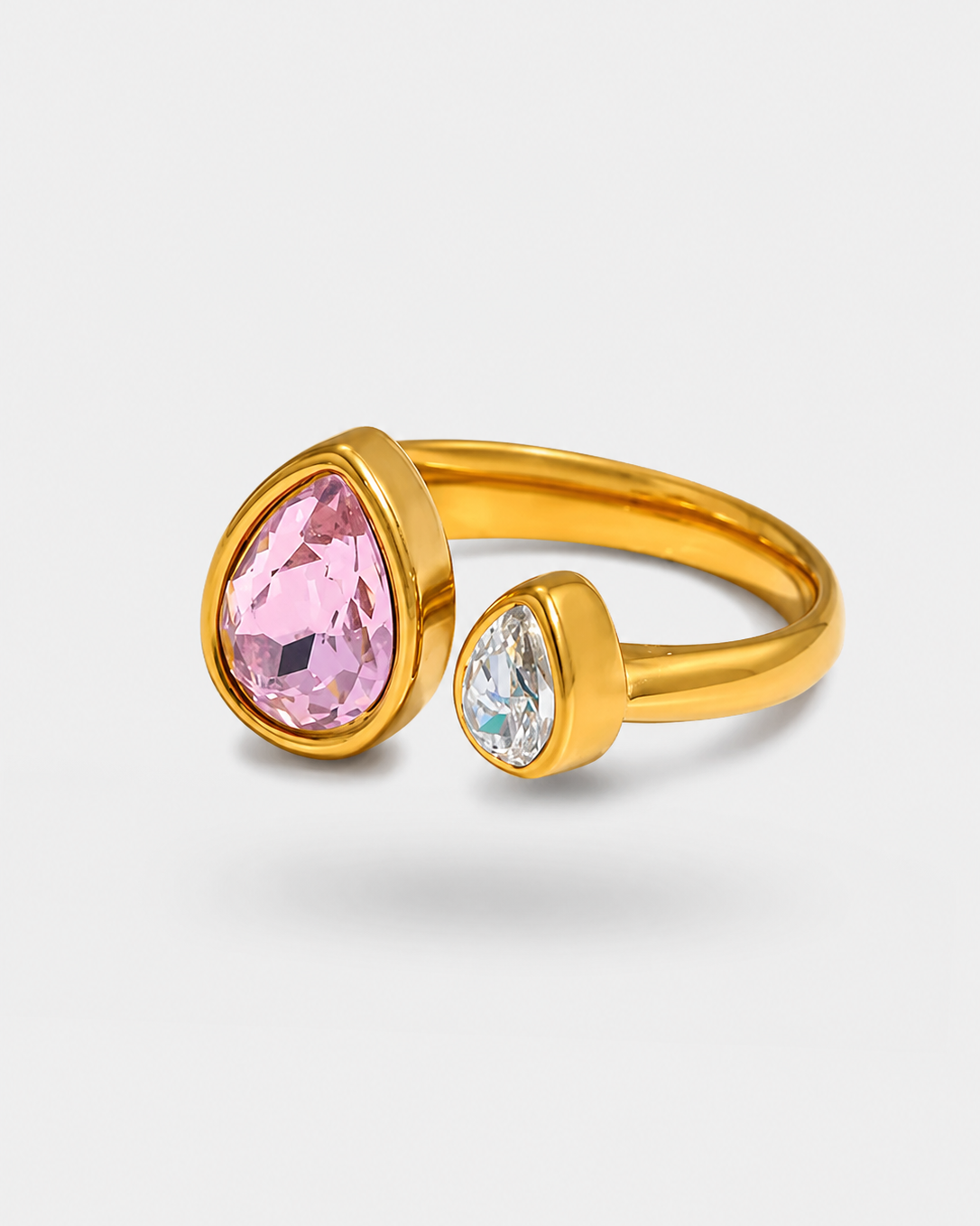 A gold ring featuring a large teardrop-shaped pink gemstone and a smaller round clear gemstone, set on a light gray background.