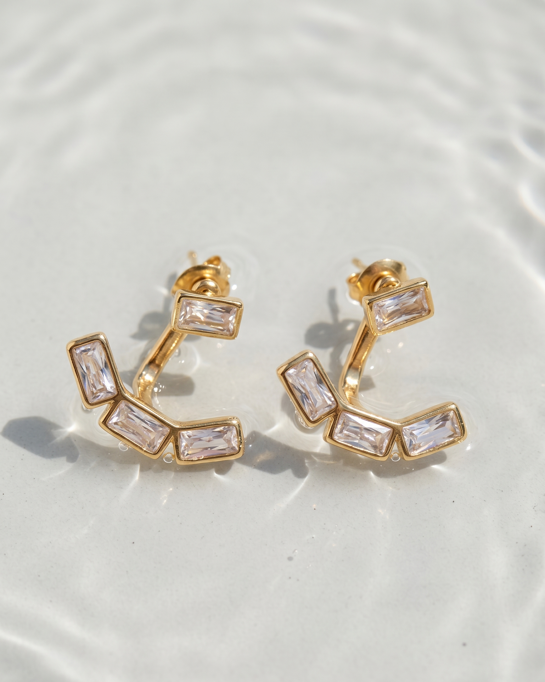 Gold hoop earrings with clear gemstones on a light background