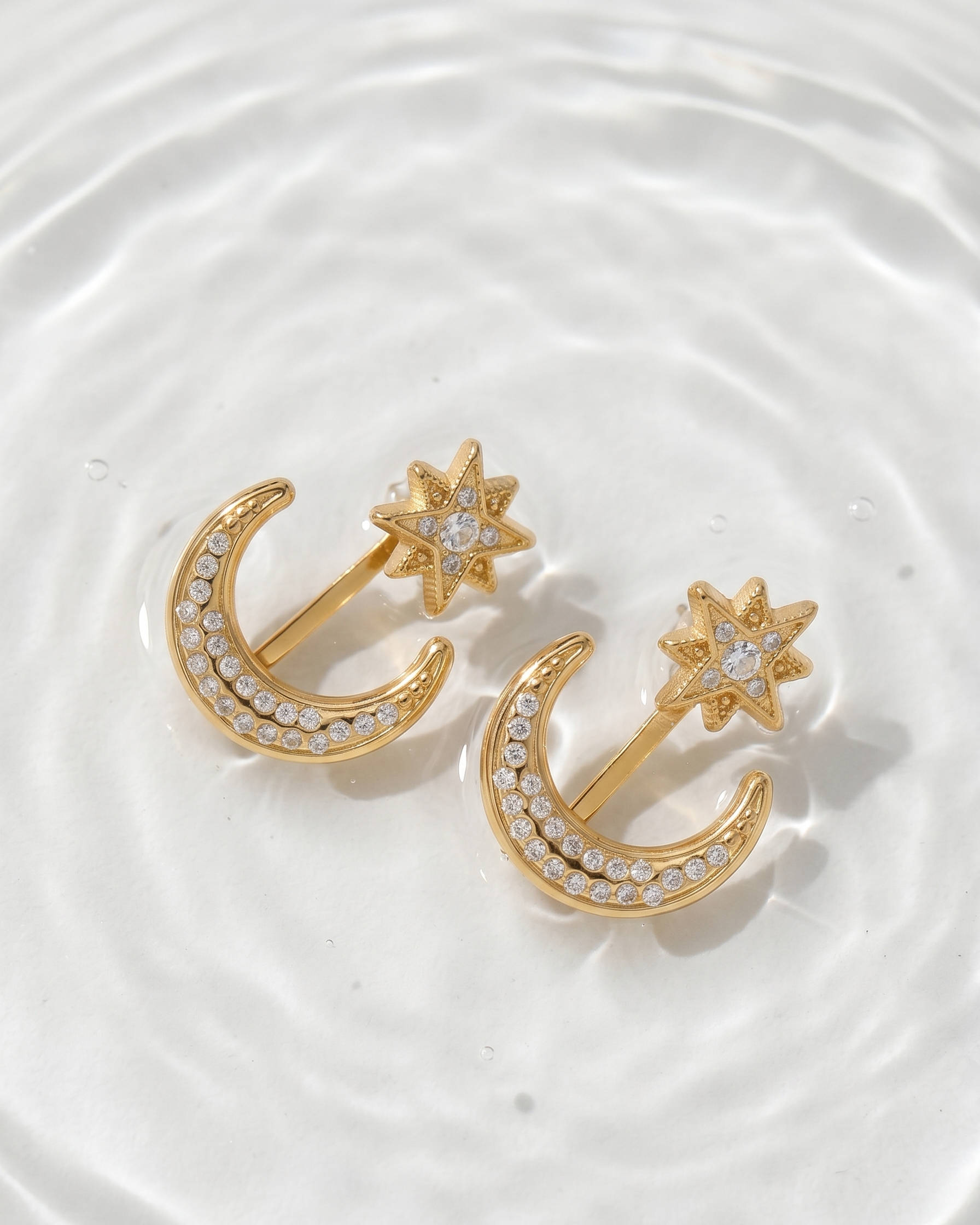 Gold earrings with star and crescent designs on a white background