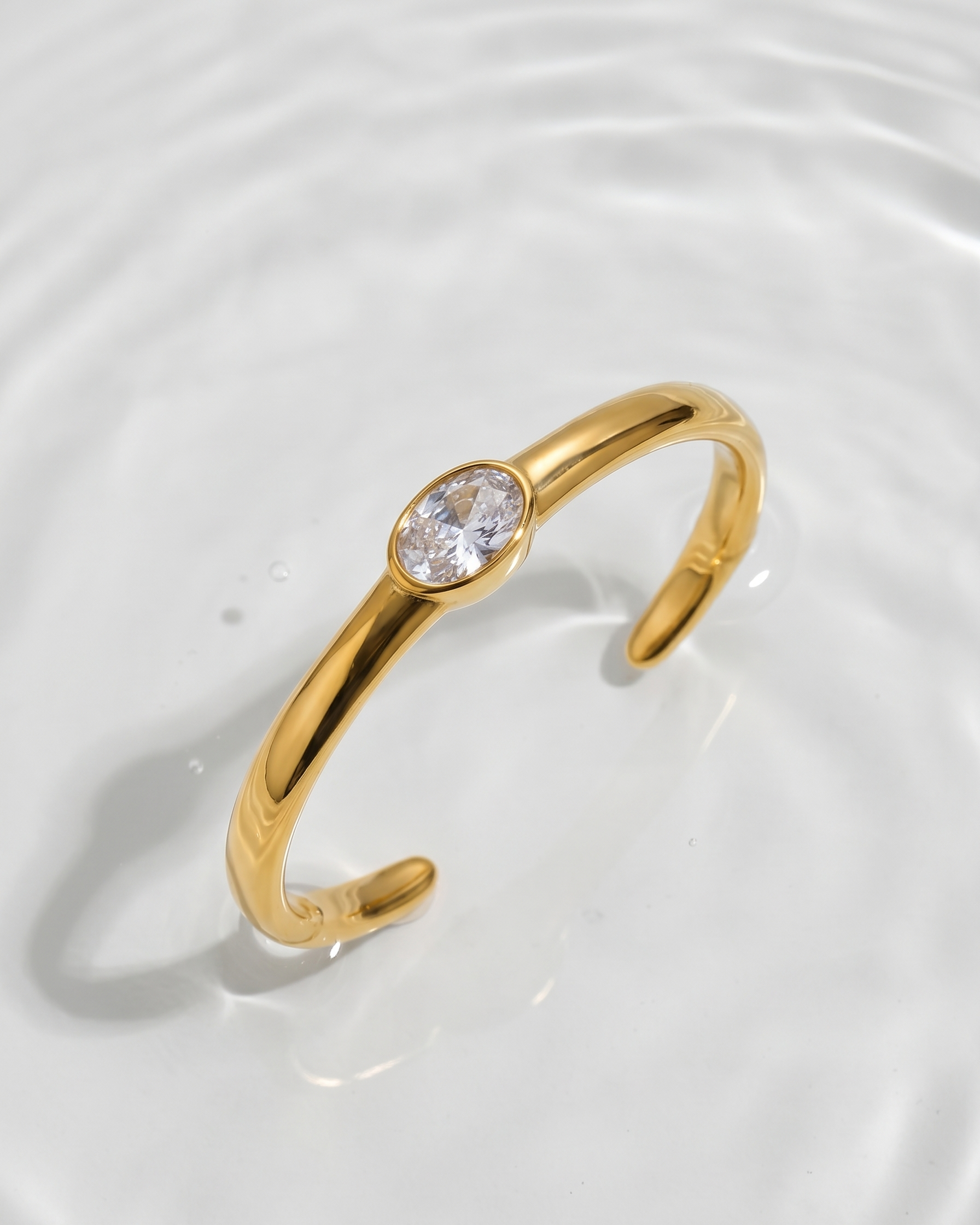 Gold open bangle with a clear gemstone on a white background