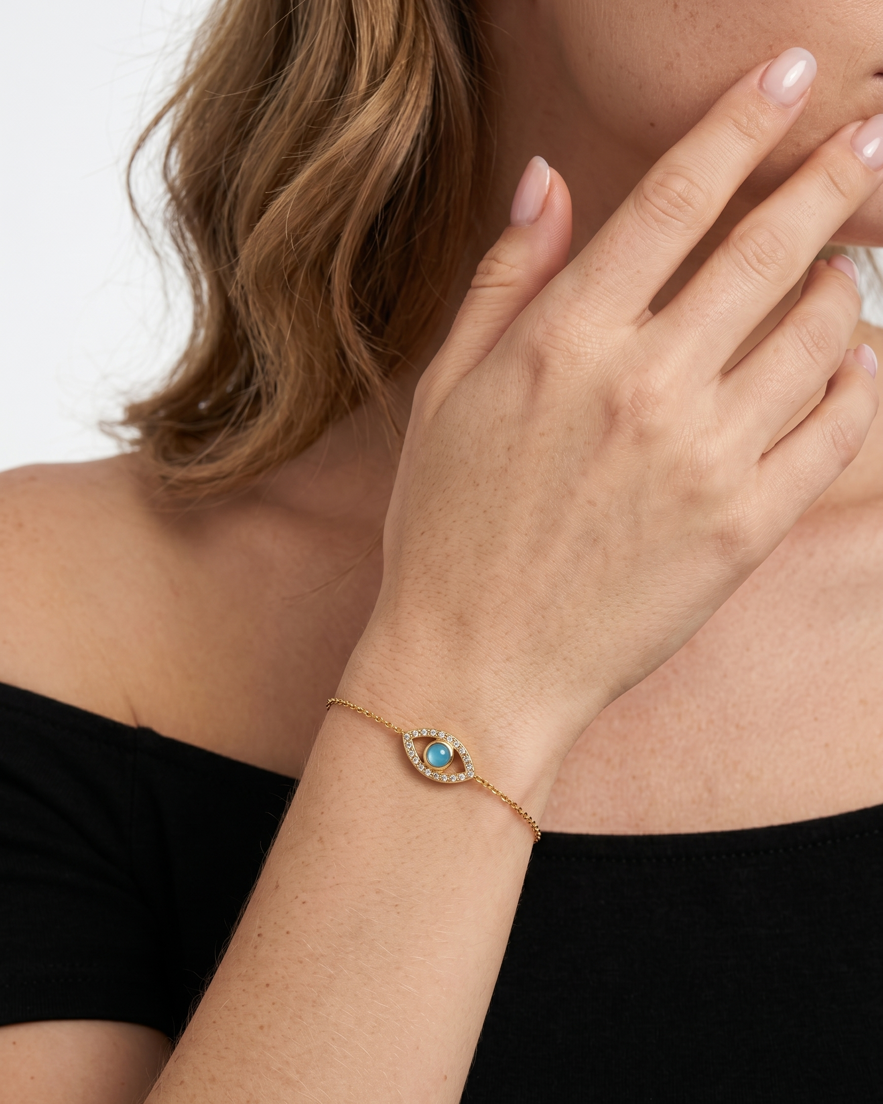 Woman wearing a gold bracelet with a blue gemstone on a plain background