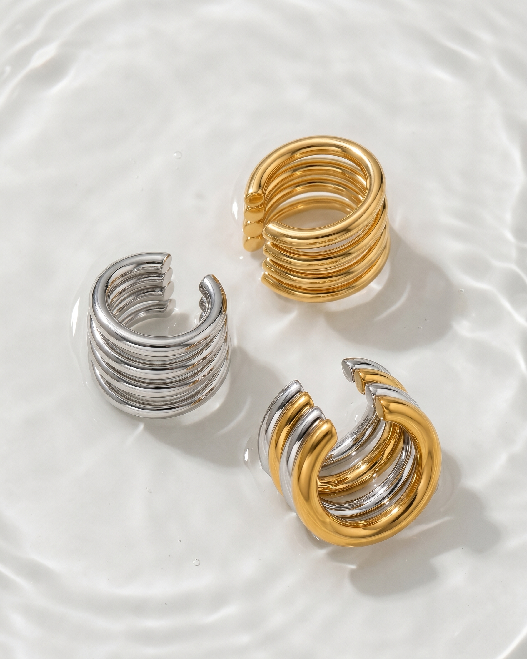 Two pairs of hoop earrings, one gold and one silver, on a white plate.
