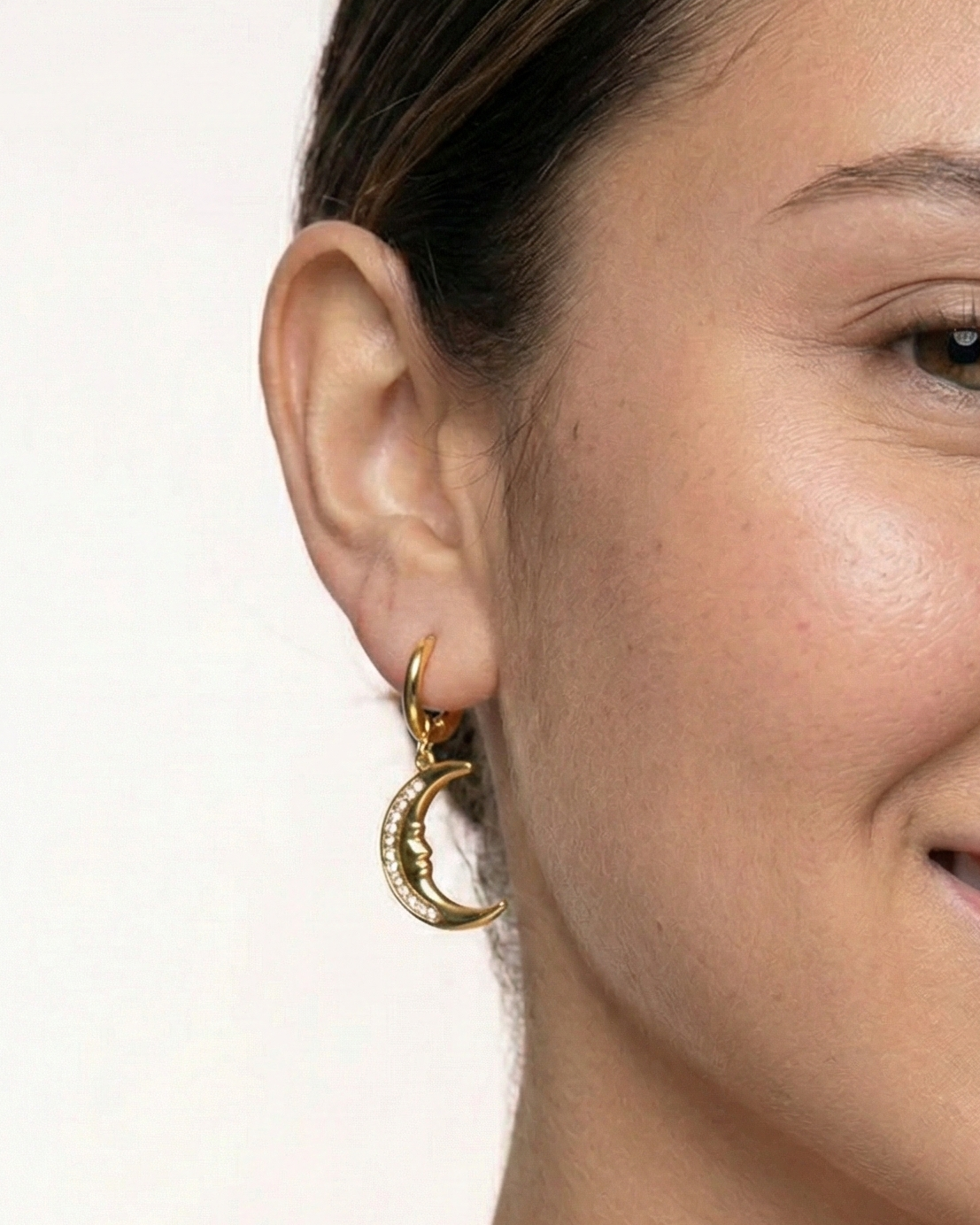 Close-up of a woman wearing gold hoop earrings on a plain background