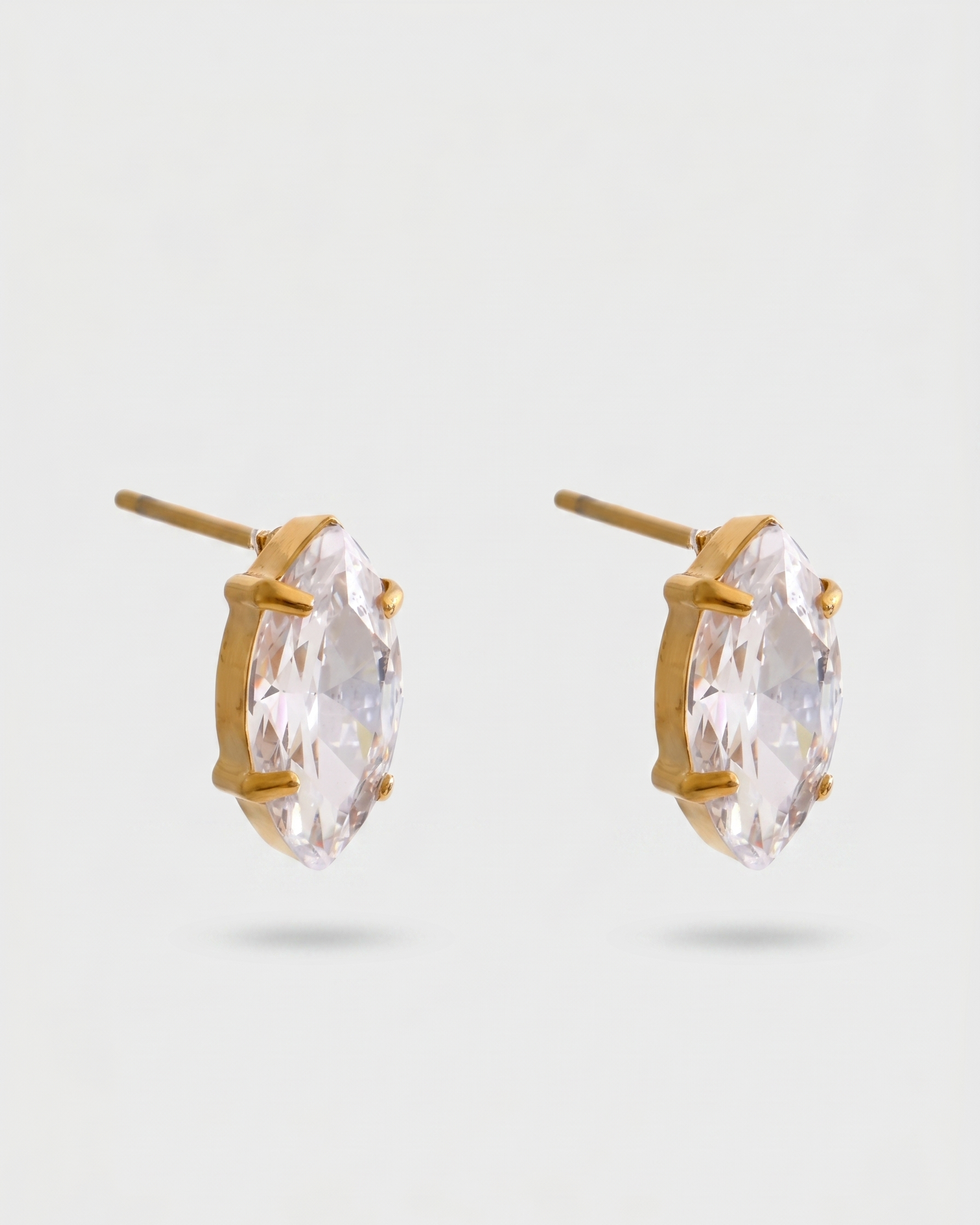 Gold earrings with clear gemstones on a light gray background