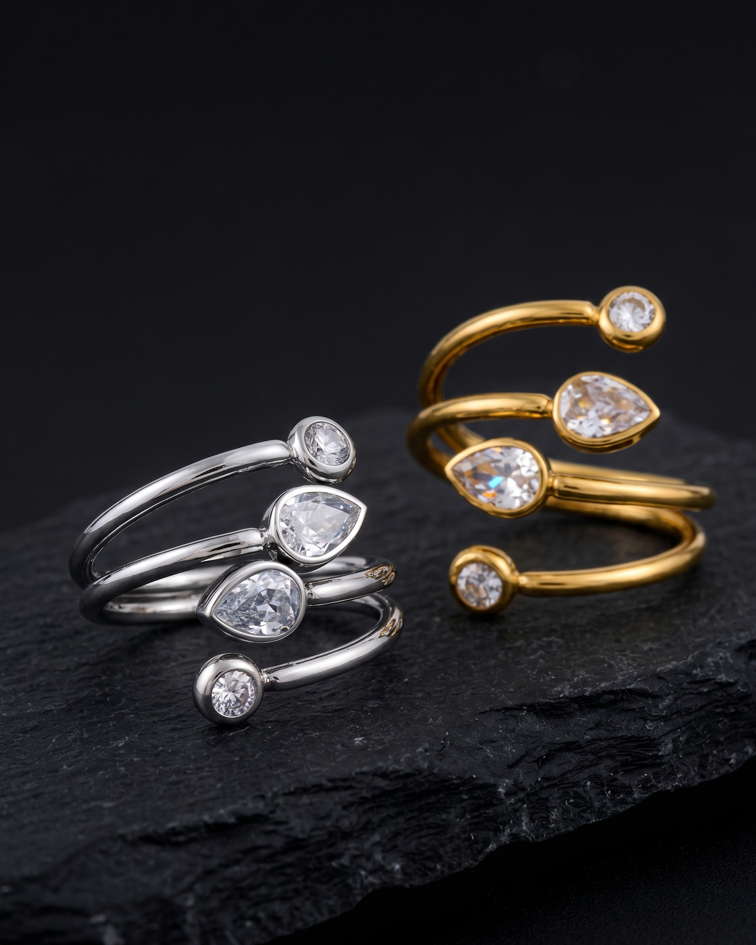 Two gold and silver open rings with teardrop-shaped gemstones on a dark surface.