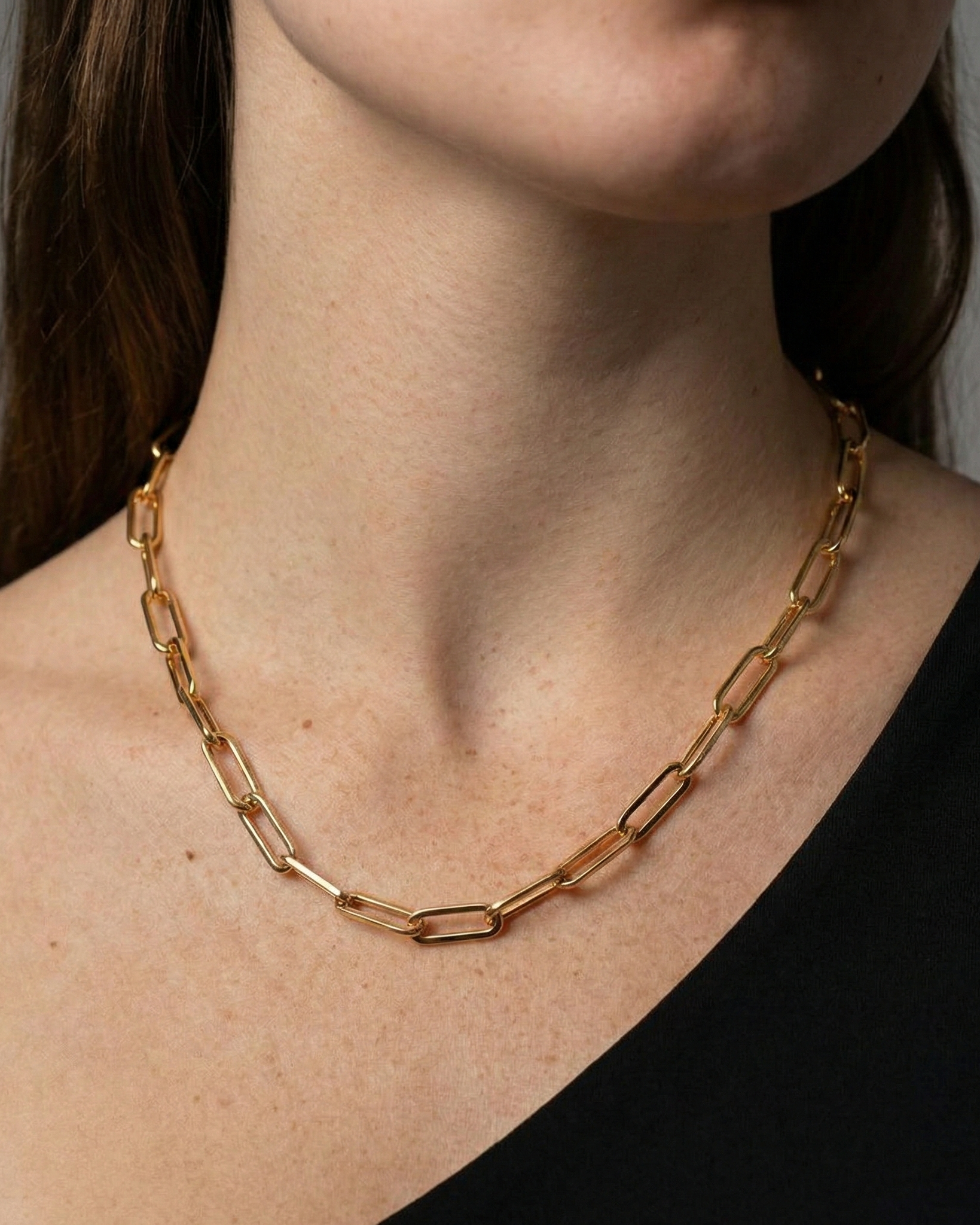 Gold chain necklace worn by a person against a neutral background