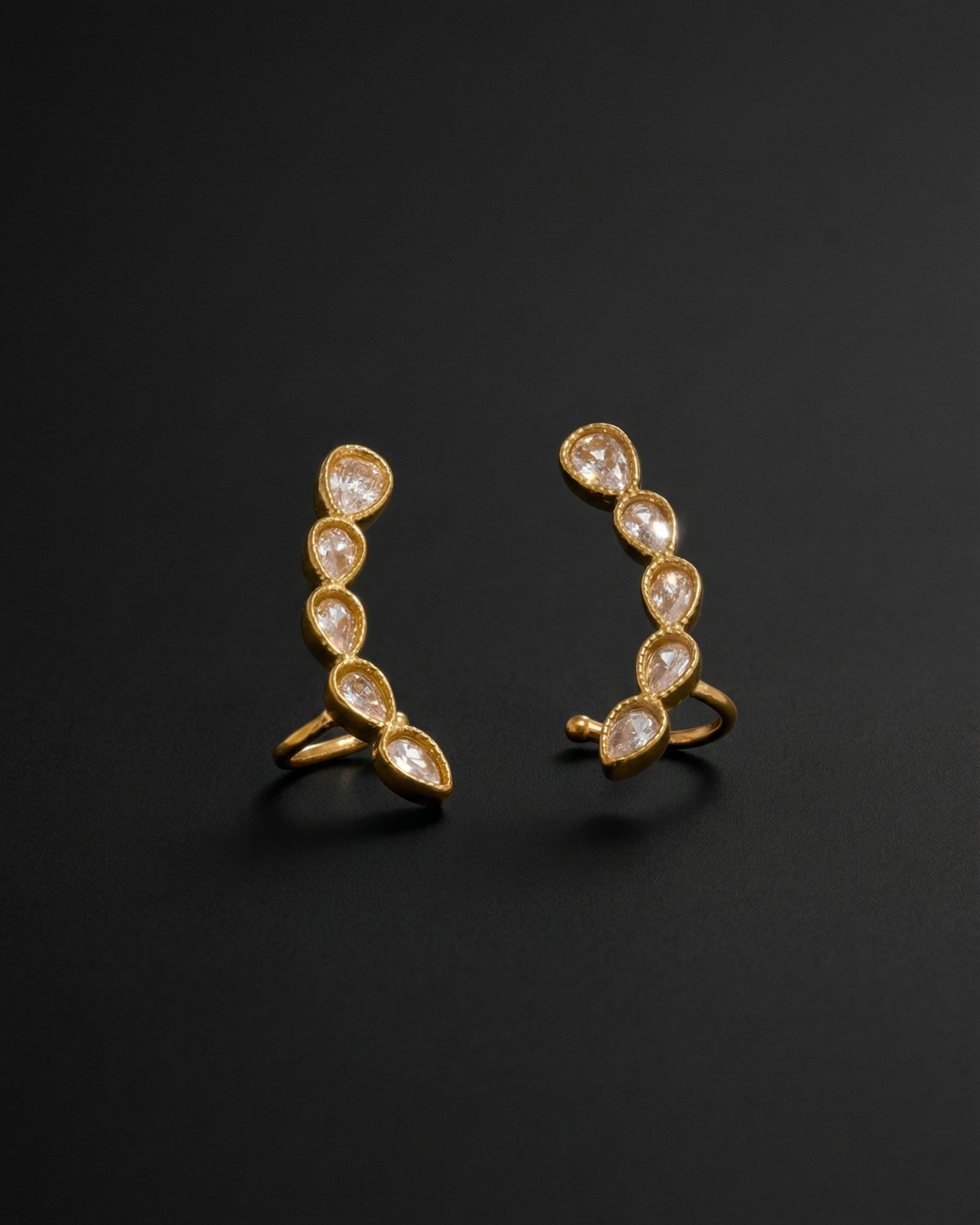 Pair of gold earrings with clear gemstones on a black background