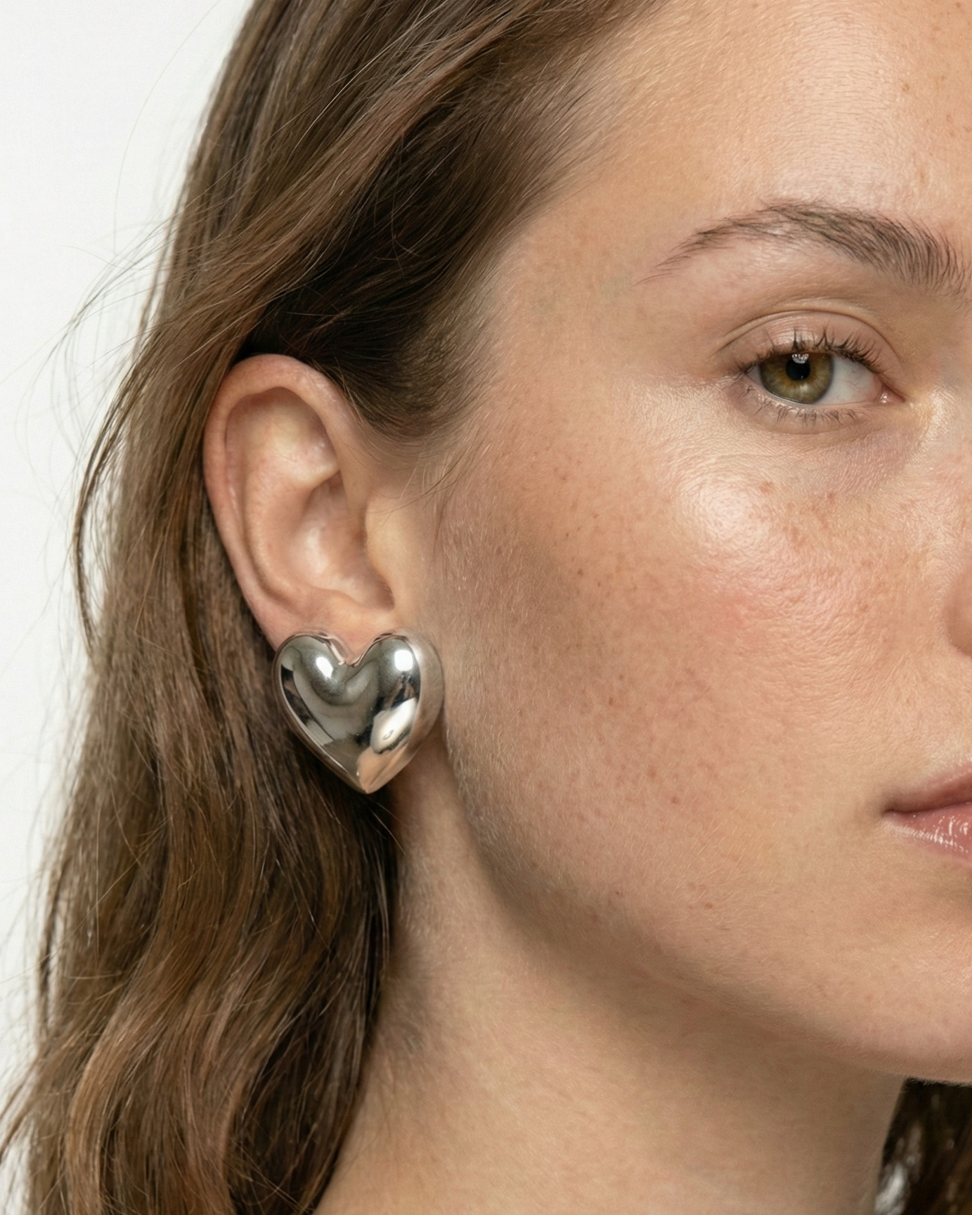 Close-up of a person wearing heart-shaped earrings on a plain background