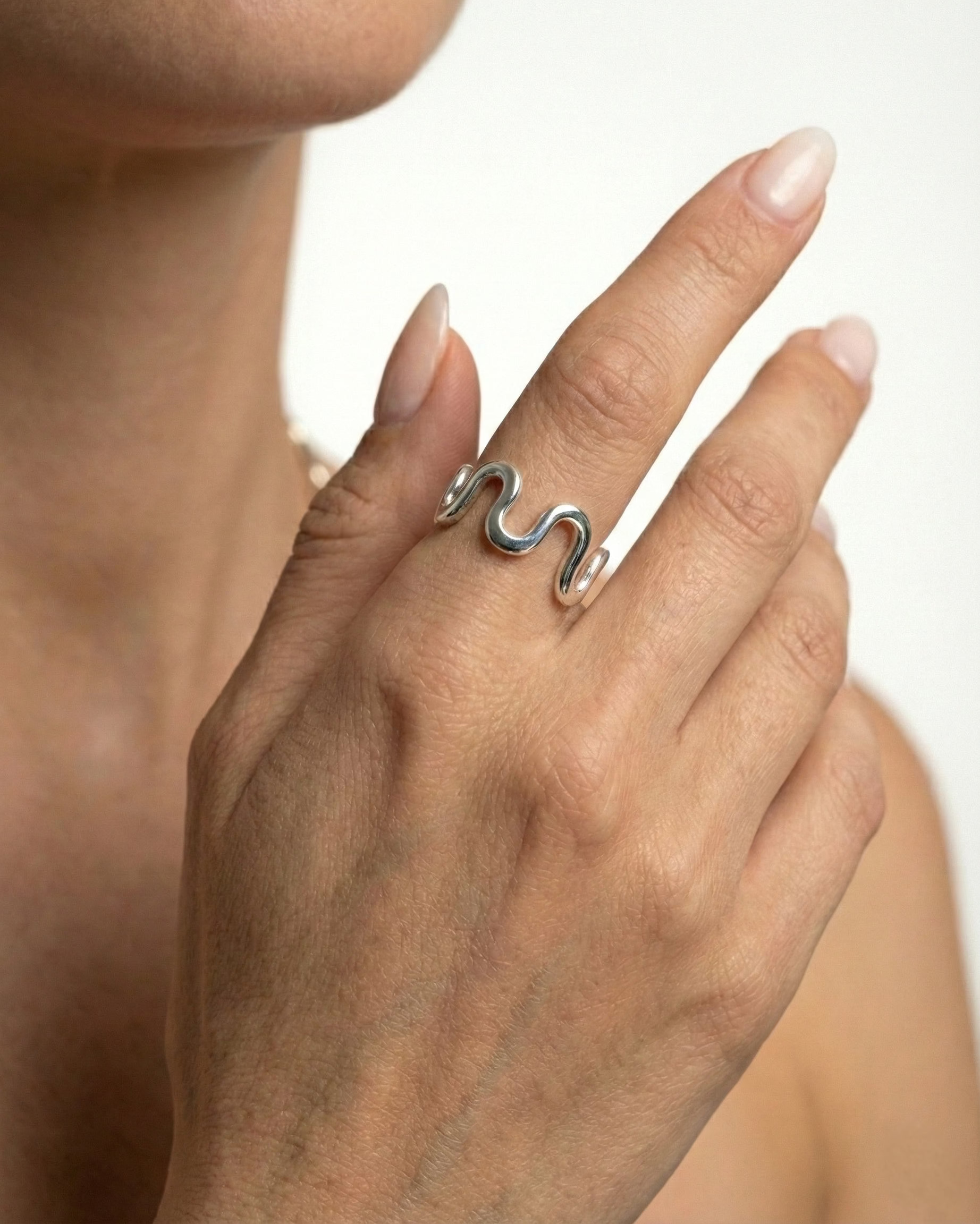 Silver ring on a finger against a neutral background