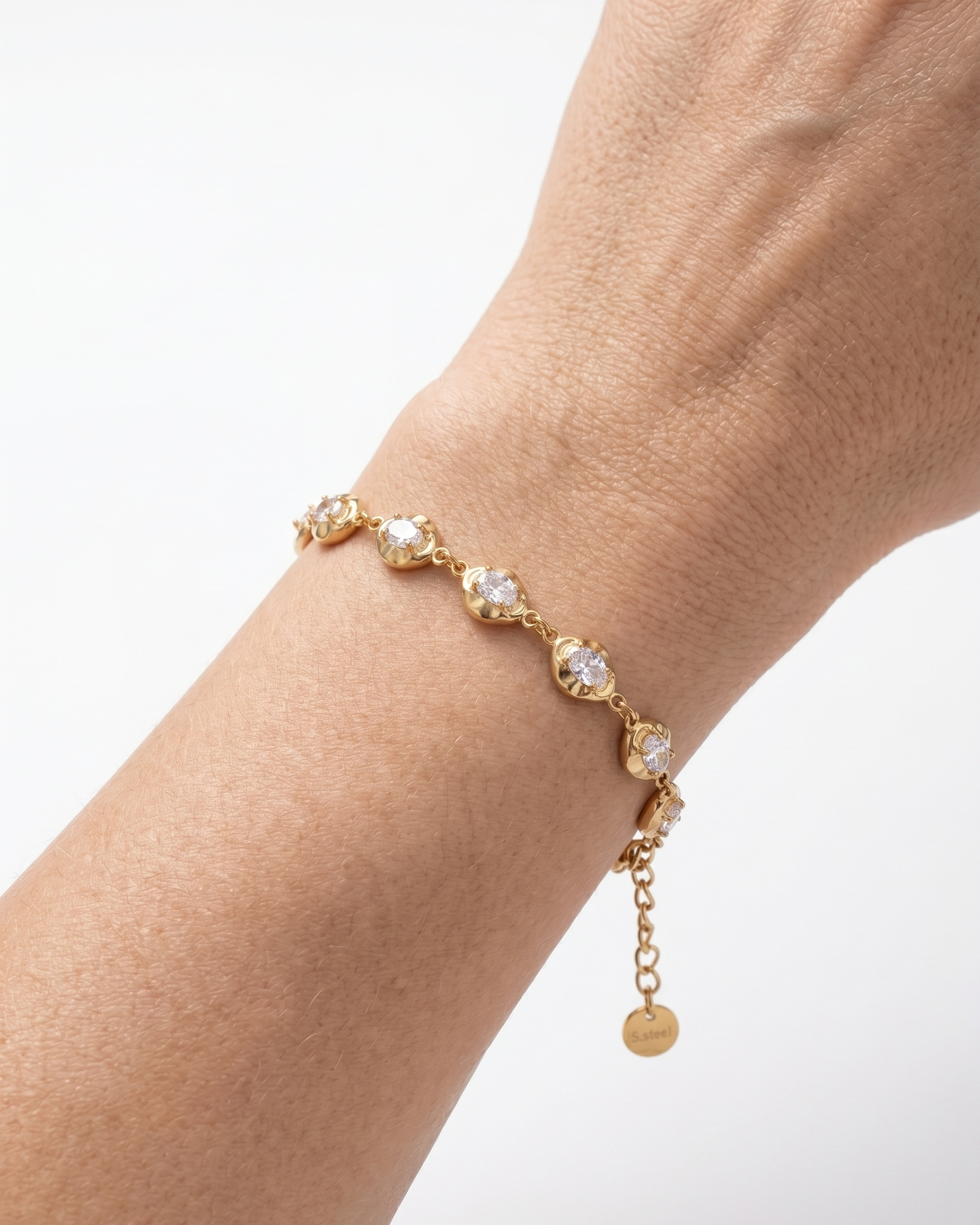Gold bracelet with clear stones on a wrist against a white background