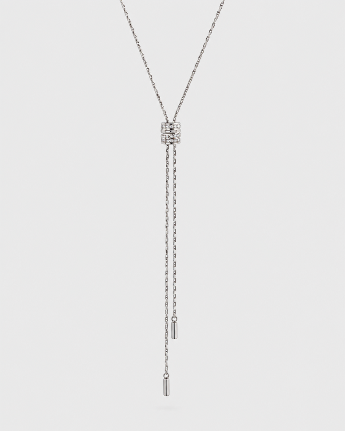 A silver-toned Y-necklace featuring a rectangular cluster of small clear stones at the center, with two dangling chains ending in polished cylindrical beads, shown against a light gray background.