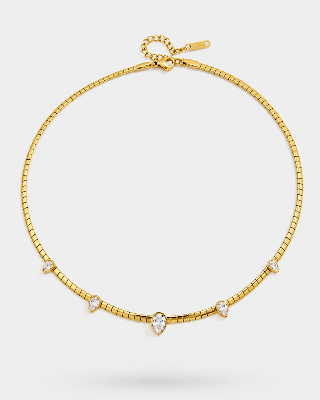 A gold chain necklace with five small clear teardrop-shaped gemstones set along the front, displayed on a light gray background.