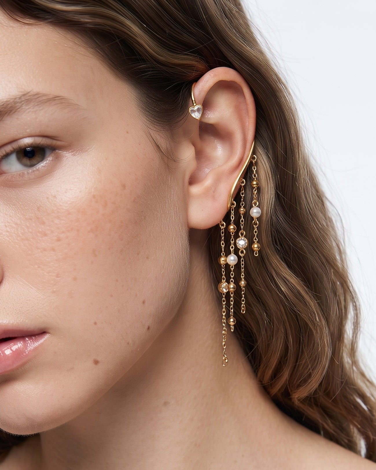 A close-up of a woman wearing a delicate gold dangle earring with small pearl-like beads, shown against a clean white background.