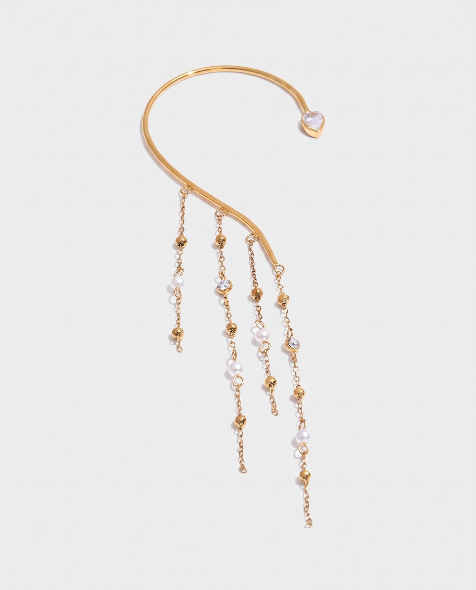 A gold-toned ear cuff earring featuring a curved main bar, a small heart-shaped pearl at the end, and three dangling chains with gold beads and clear faceted pearls, shown on a light gray background.