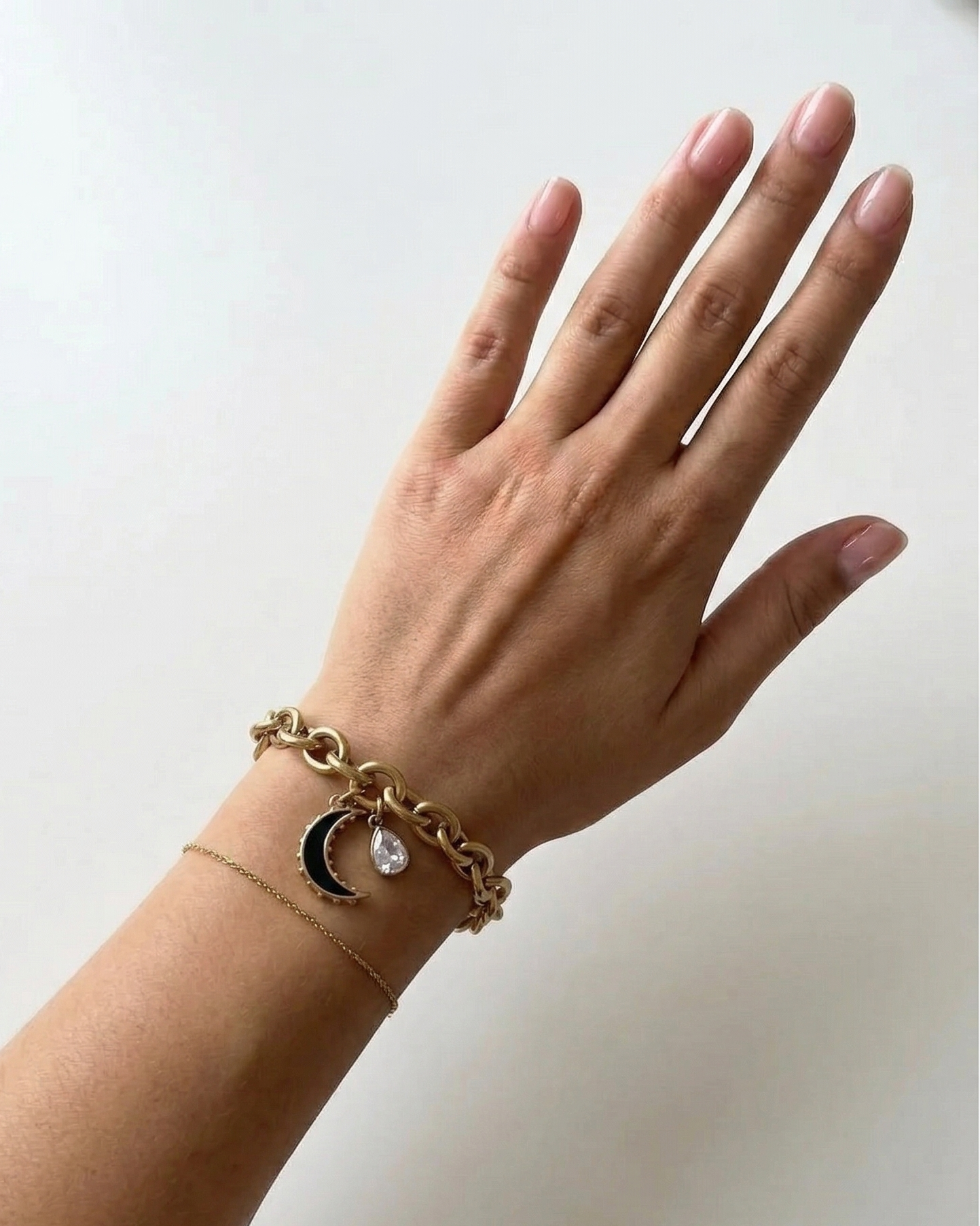Hand wearing a gold bracelet with moon and star charms on a white background